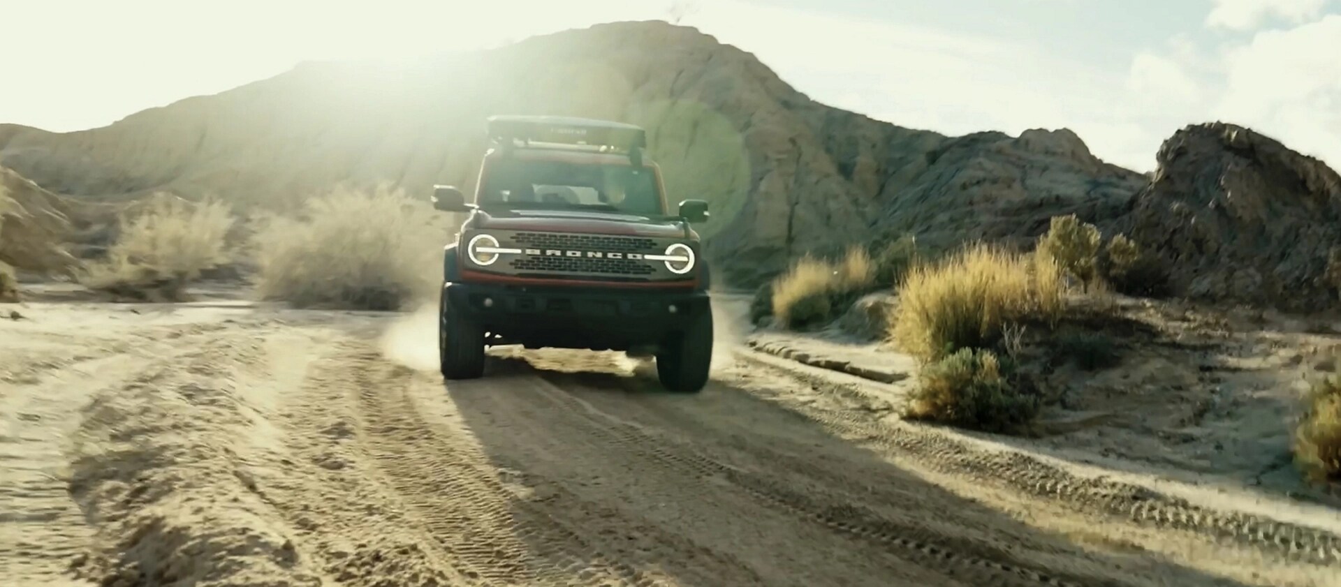 A 2026 Ford Bronco® SUV being driven on a dirt trail through a stark, dusty landscape
