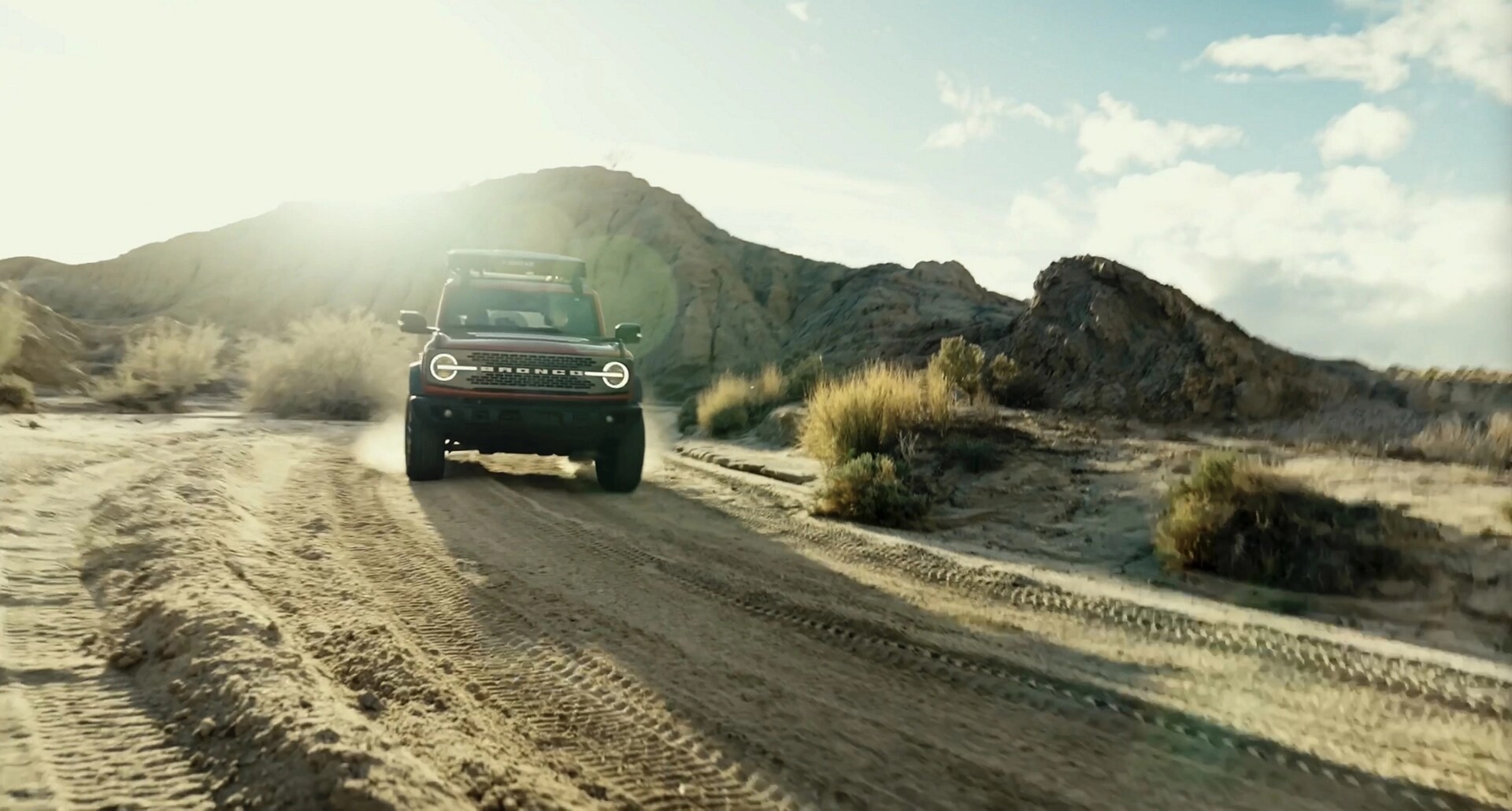 A 2026 Ford Bronco® SUV being driven on a dirt trail through a stark, dusty landscape