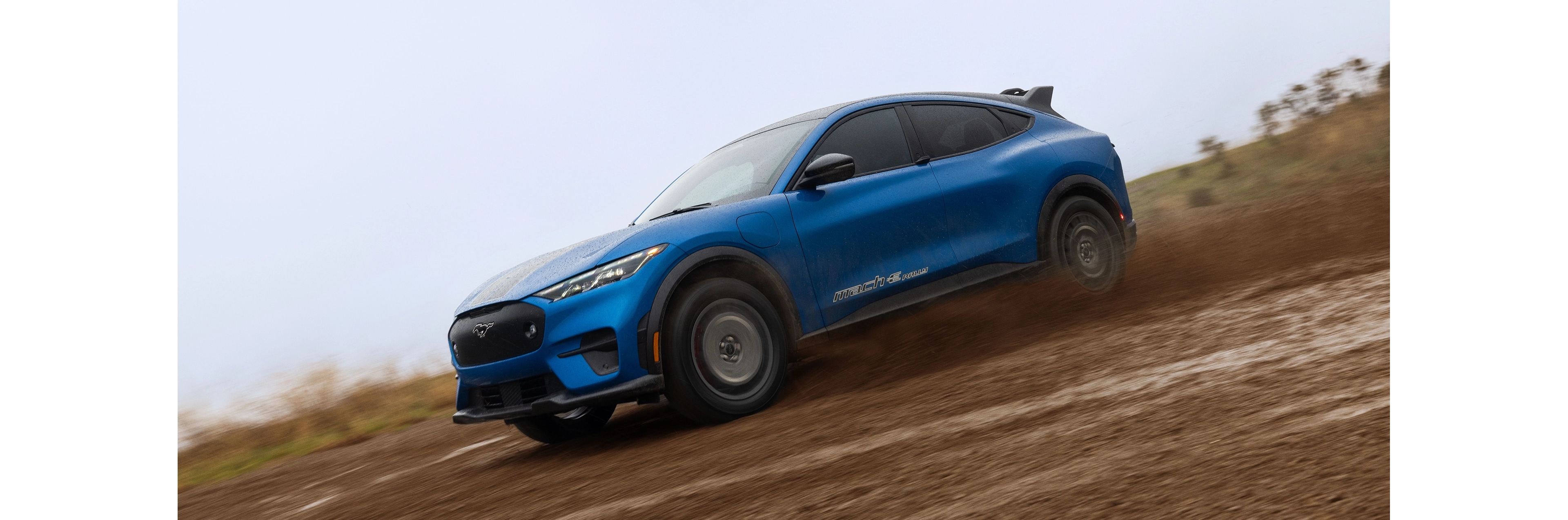 A blue Mustang Mach-E powering through a muddy trail. 