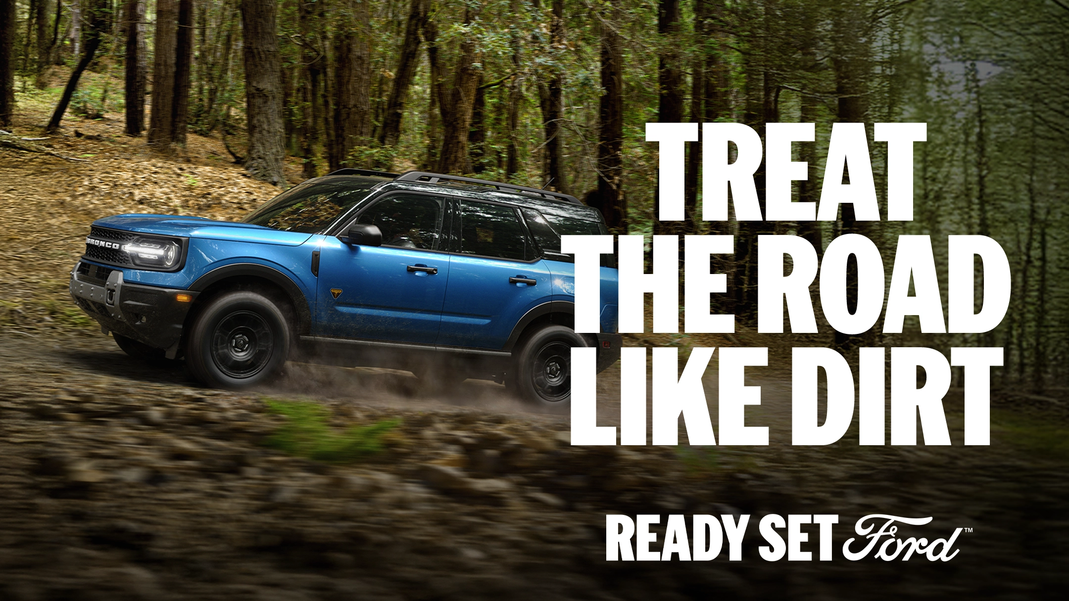 Side profile view of a blue Bronco Sport off-roading on a dirt road through a forest.  