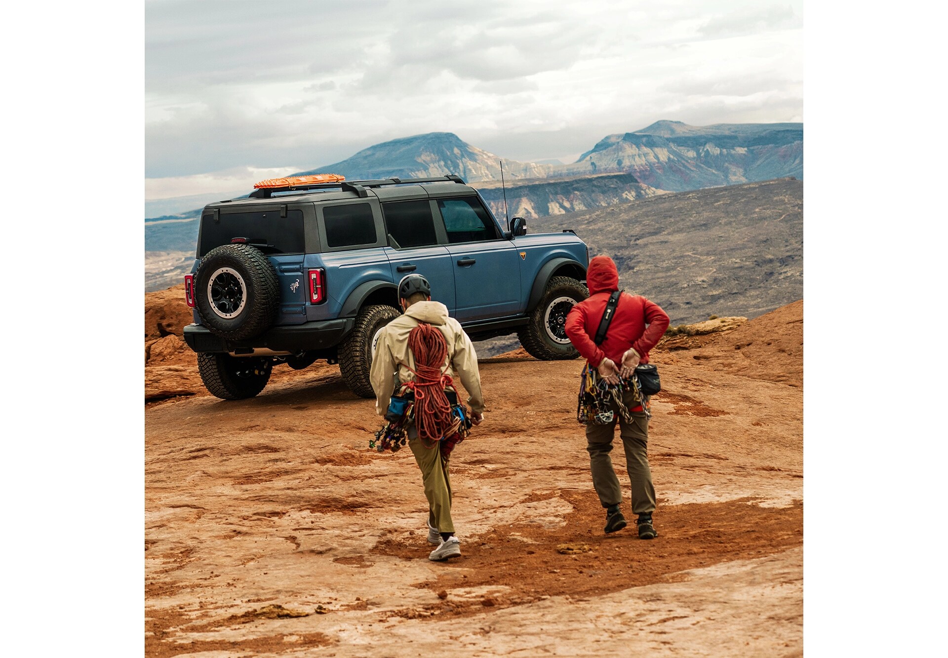 Two male climbers walking towards a Ford Bronco parked on rocky terrain.