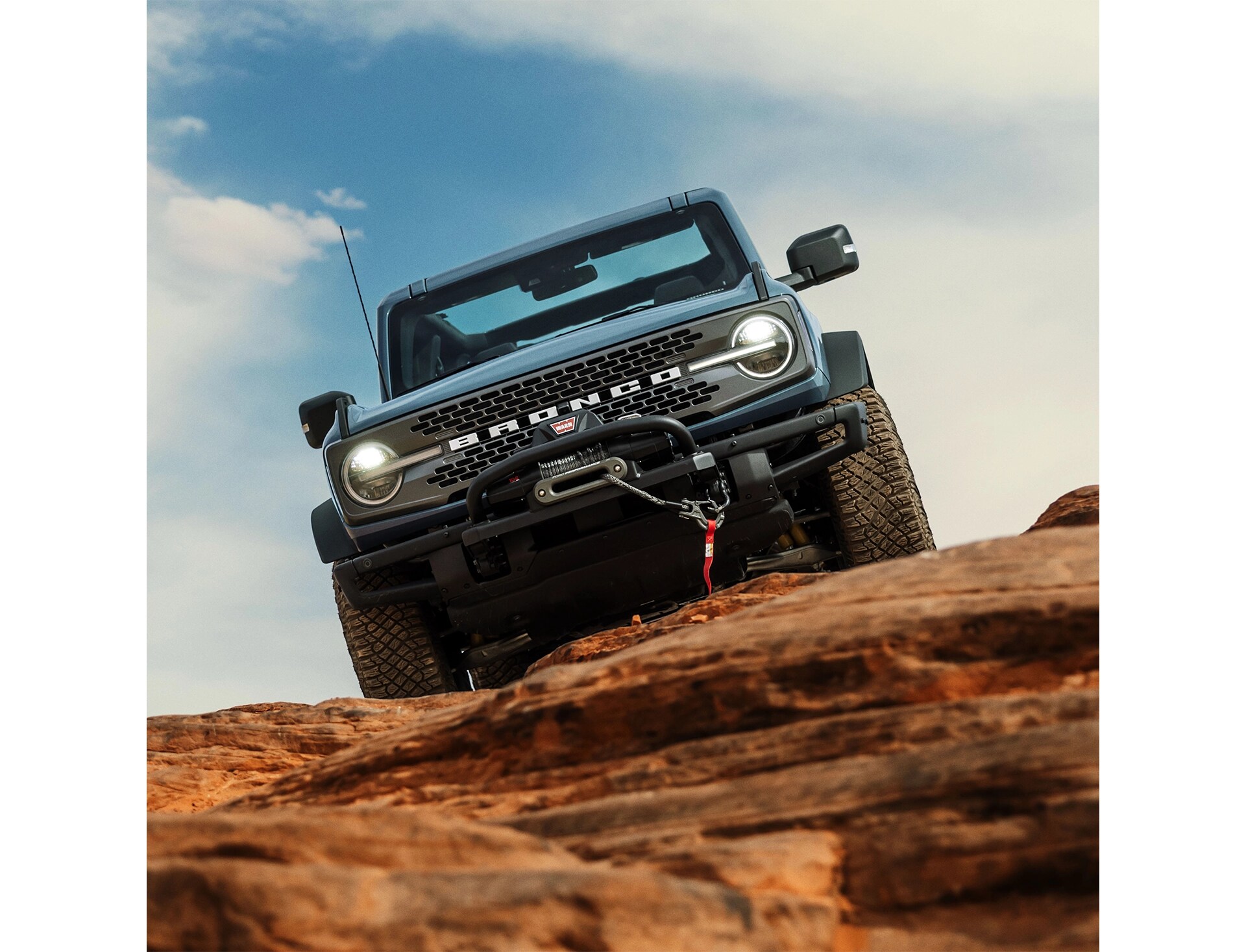 Front view of a grey-blue Ford Bronco parked atop rocky terrain.