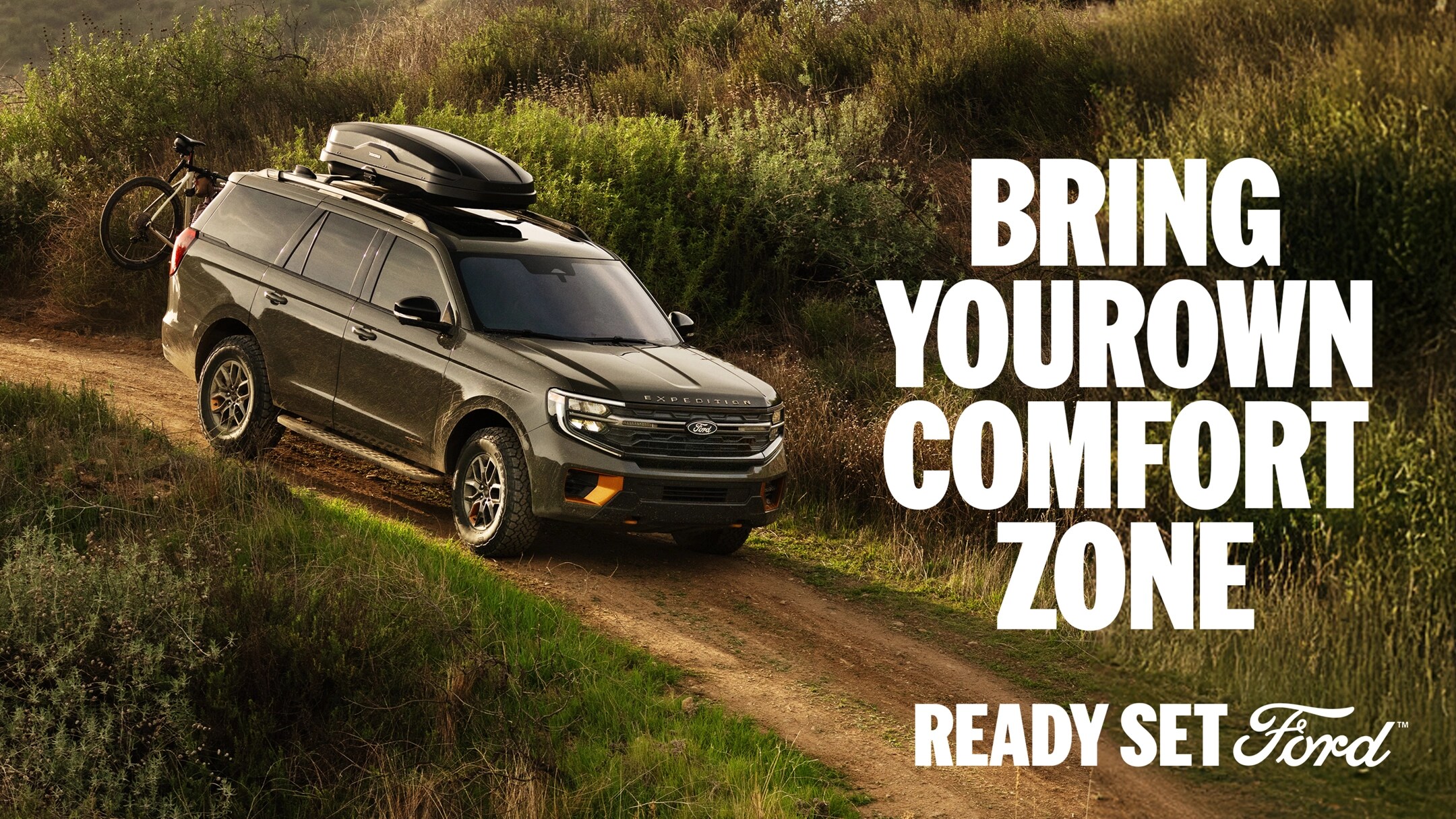 A side profile view of the 2025 Expedition on a dirt trail with a mountain bike mounted on the back. White text “Bring Your Own Comfort Zone” appears in the top-right corner.