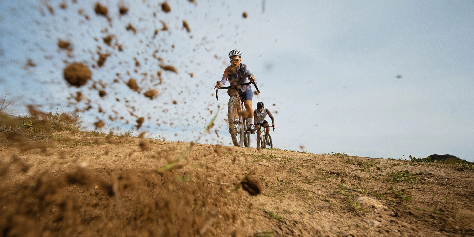 Two mountain bikers, one behind the other, travel along rocky ground. 