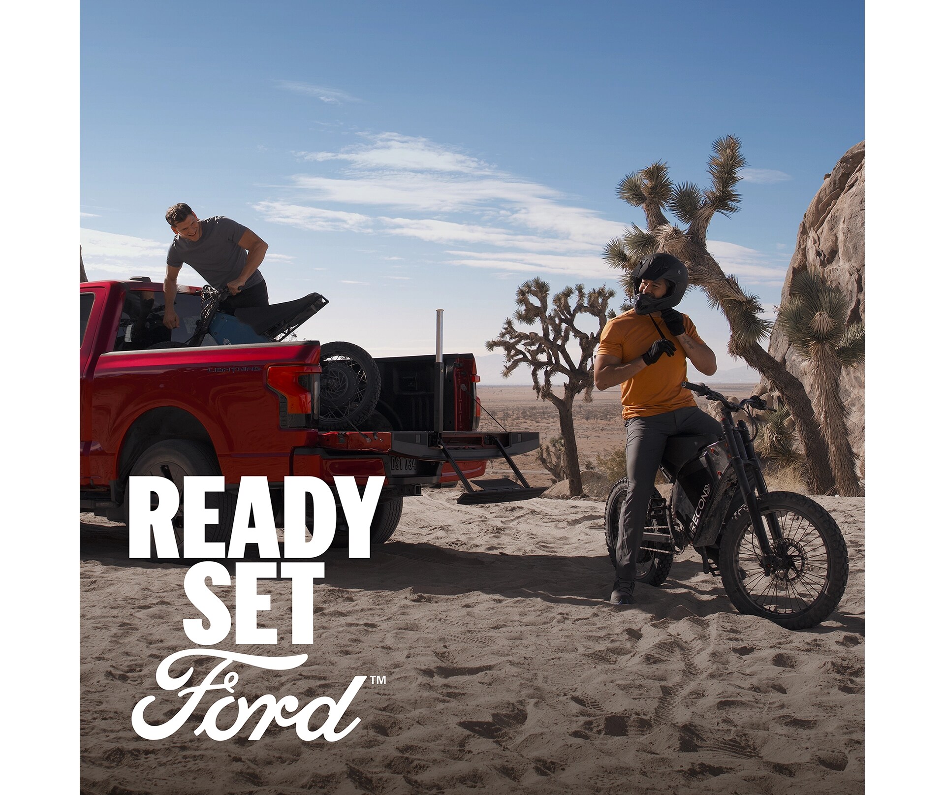 A rear view of a red F-150 Lightning with two men gearing up for dirt biking — one unloading a bike from the truck bed. In the left-hand corner white text appears, “Ready Set Ford”. 