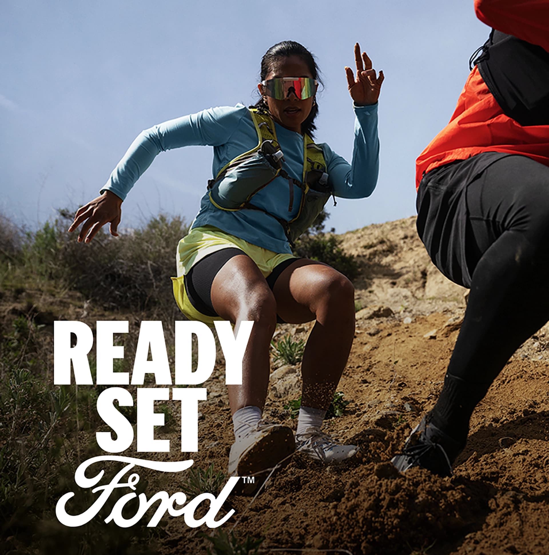 Two people descending a steep dirt hill.  White text “Ready Set Ford” appears in the lower right-hand corner.