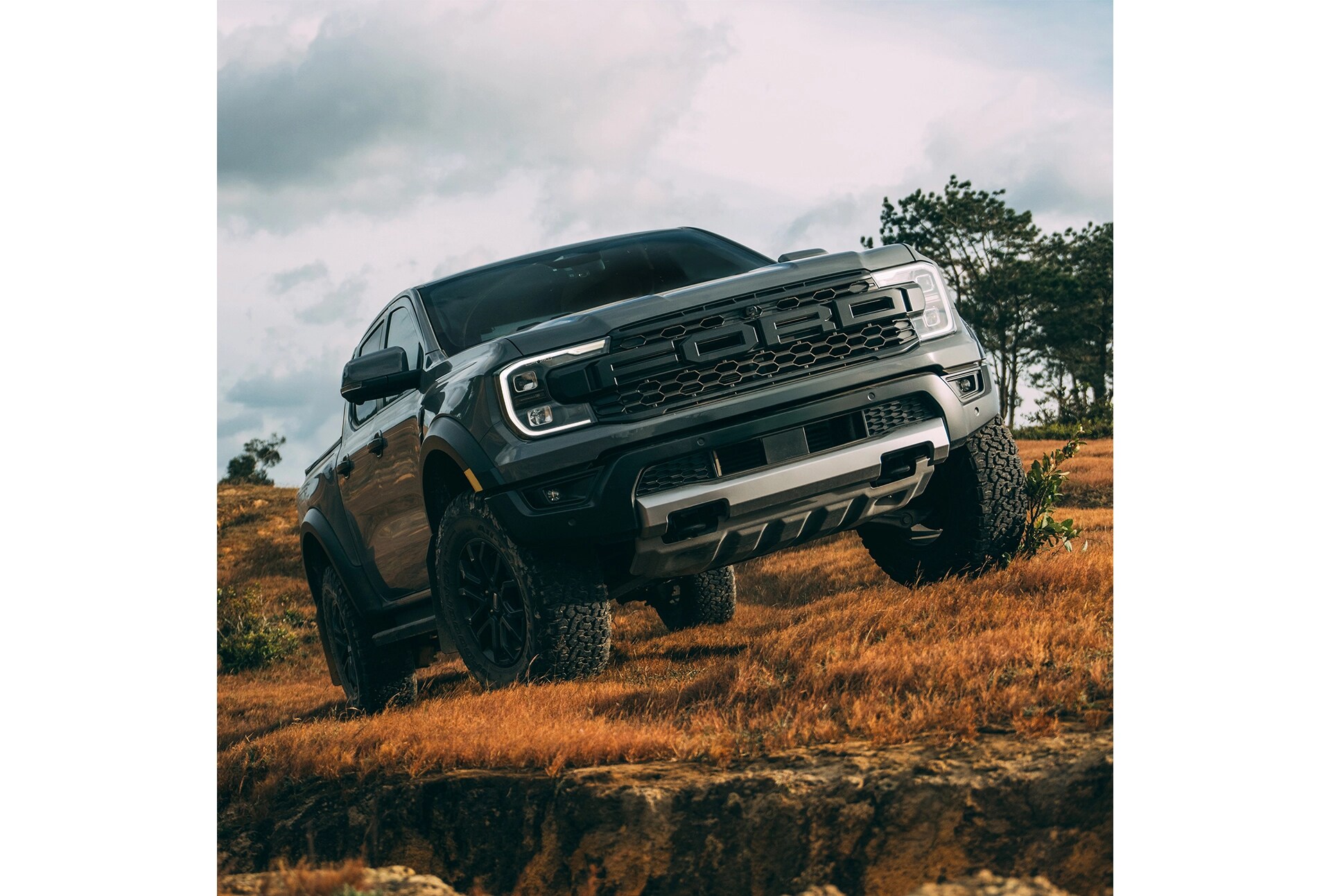 Three-quarter front view of a grey Ford Ranger Raptor off-roading through an open field. 