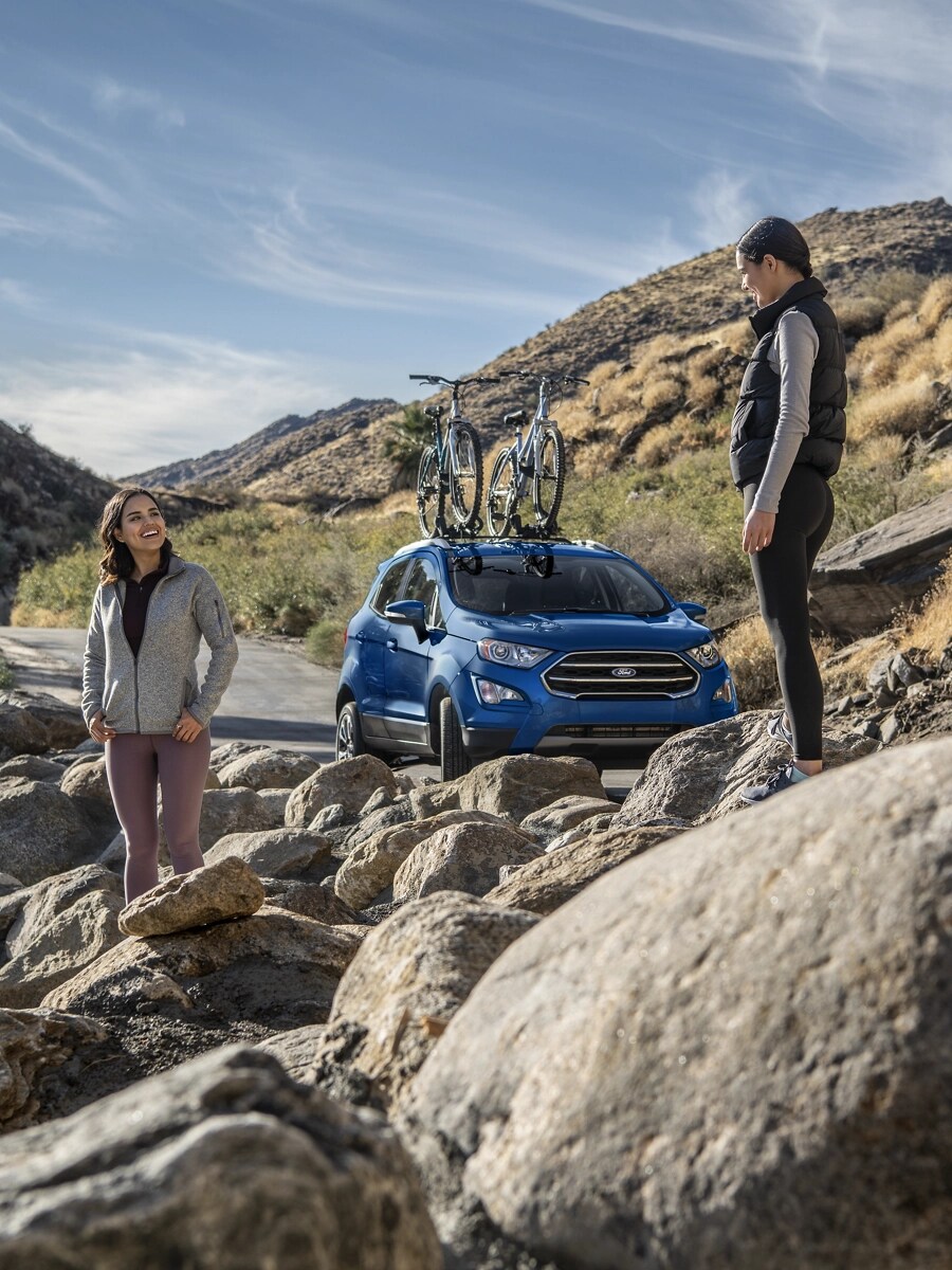 Two young women stand in a rocky landscape near a Ford crossover