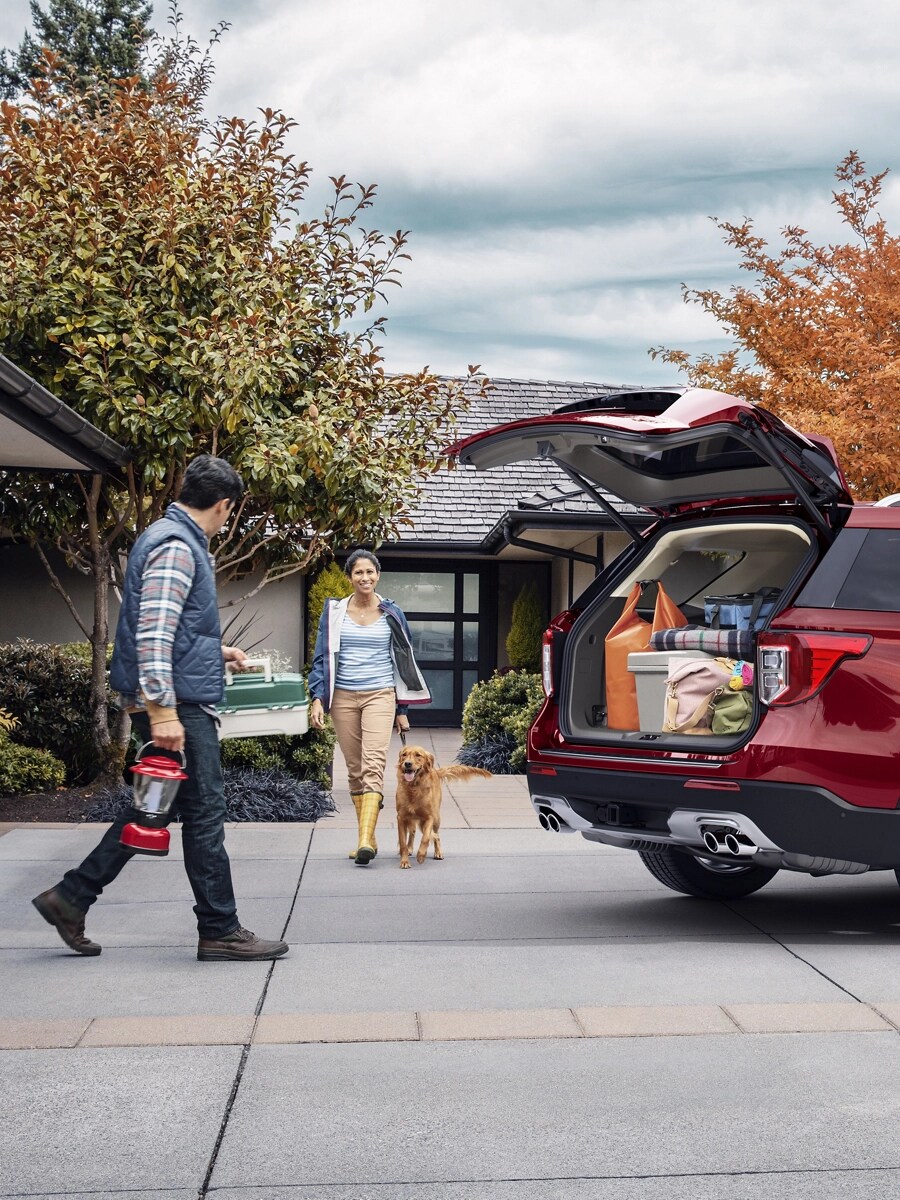 A couple with dog walk towards a Ford SUV