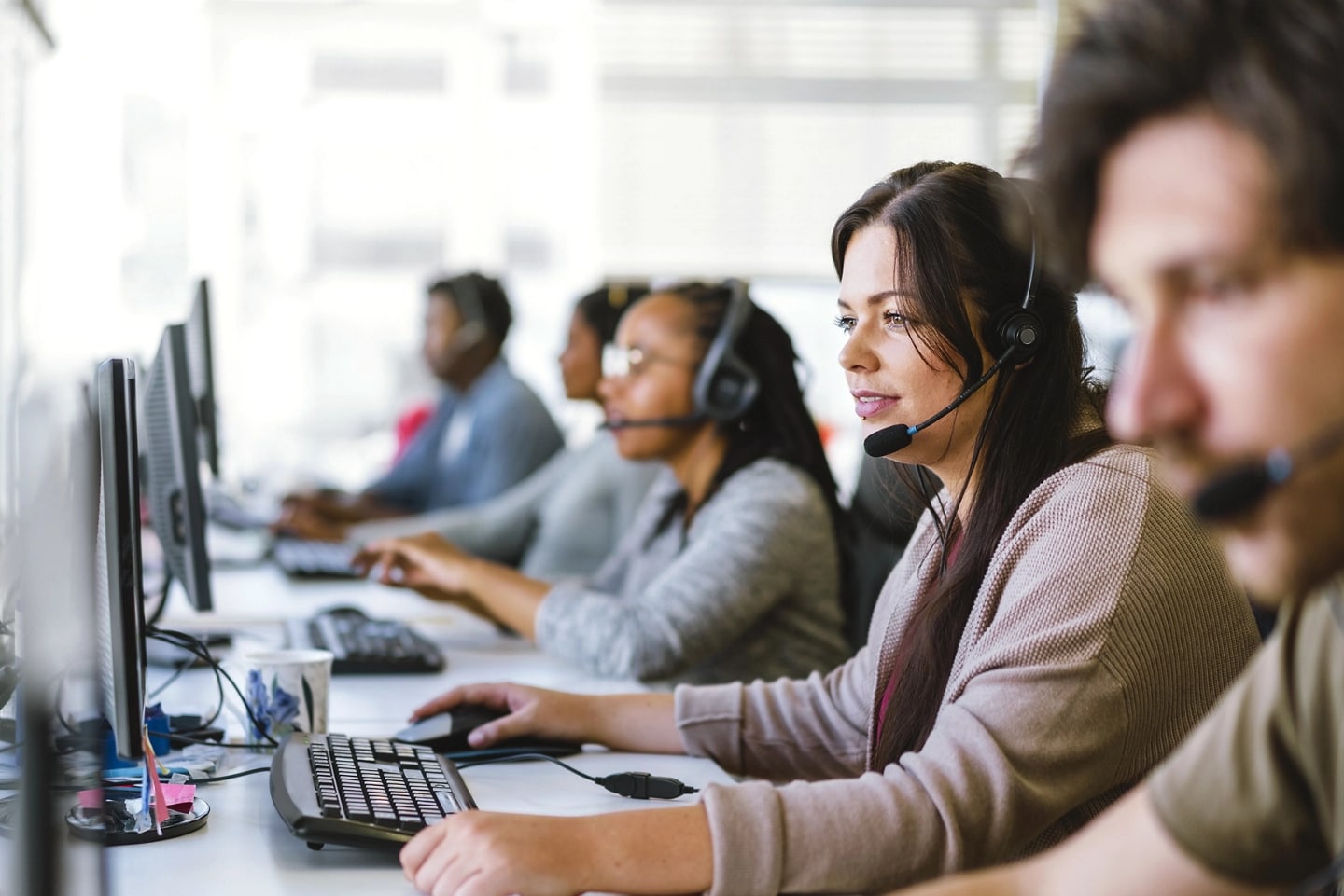 A team of customer service agents, all wearing headsets, seated at a row of computers