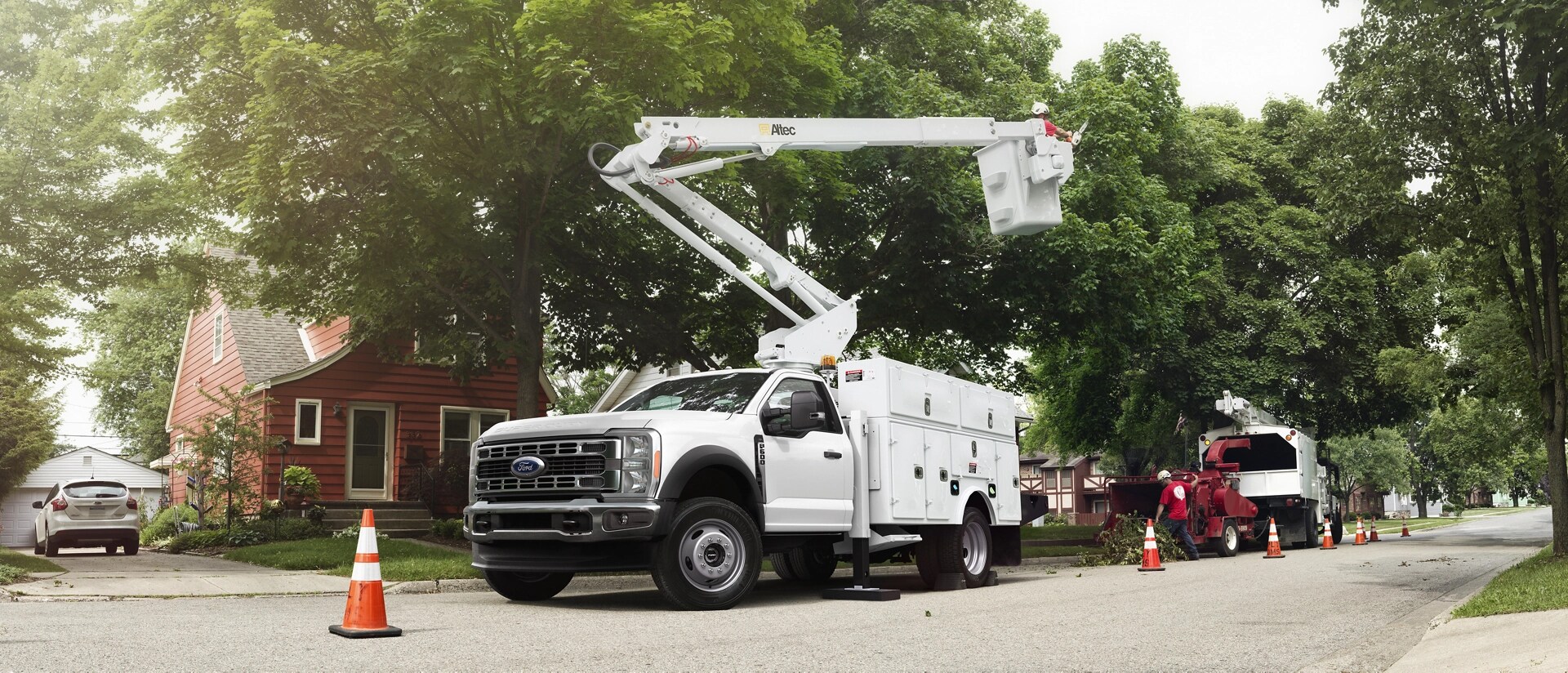 A White 2026 Ford Super Duty® Chassis Cab with a boom extension and utility box trimming tall trees
