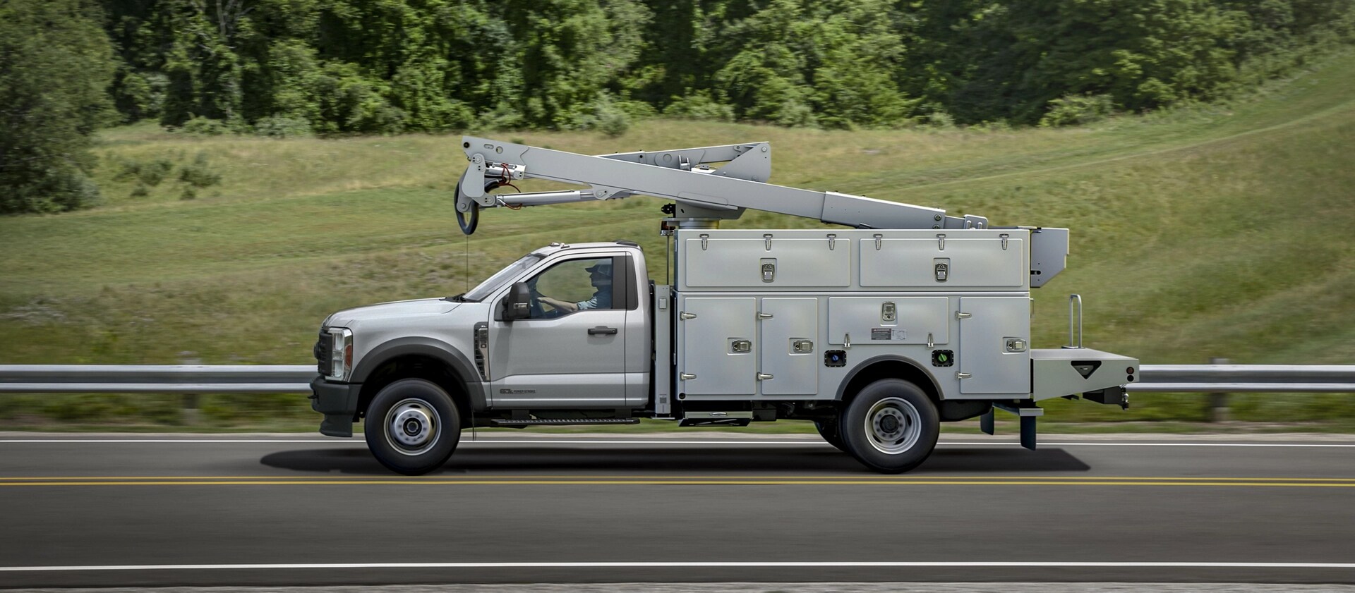 A 2026 Ford Super Duty® Chassis Cab with a boom extension and utility box driving down a road