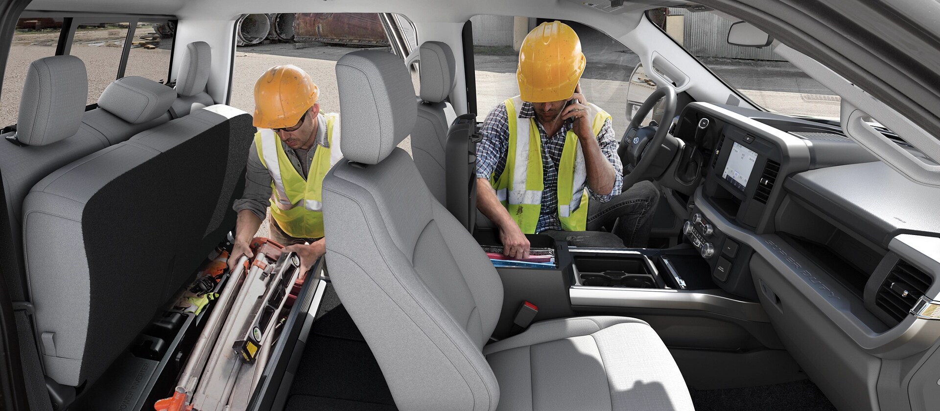 Two workers in hard hats access the storage areas inside the cab of the 2026 Ford Super Duty® Chassis Cab