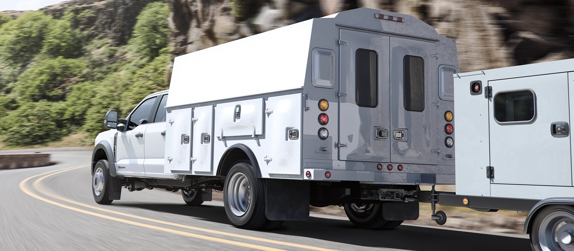A 2026 Ford Super Duty® Chassis Cab with a utility box being driven up a road alongside a mountain