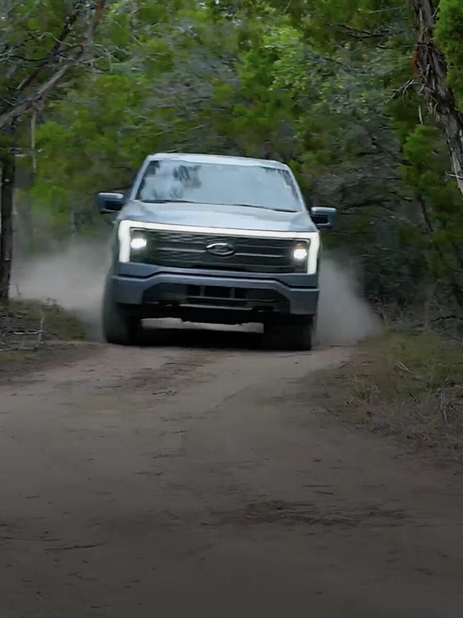 F-150 Lightning driving on a dirt trail. Mustang Mach-E driving on a highway.