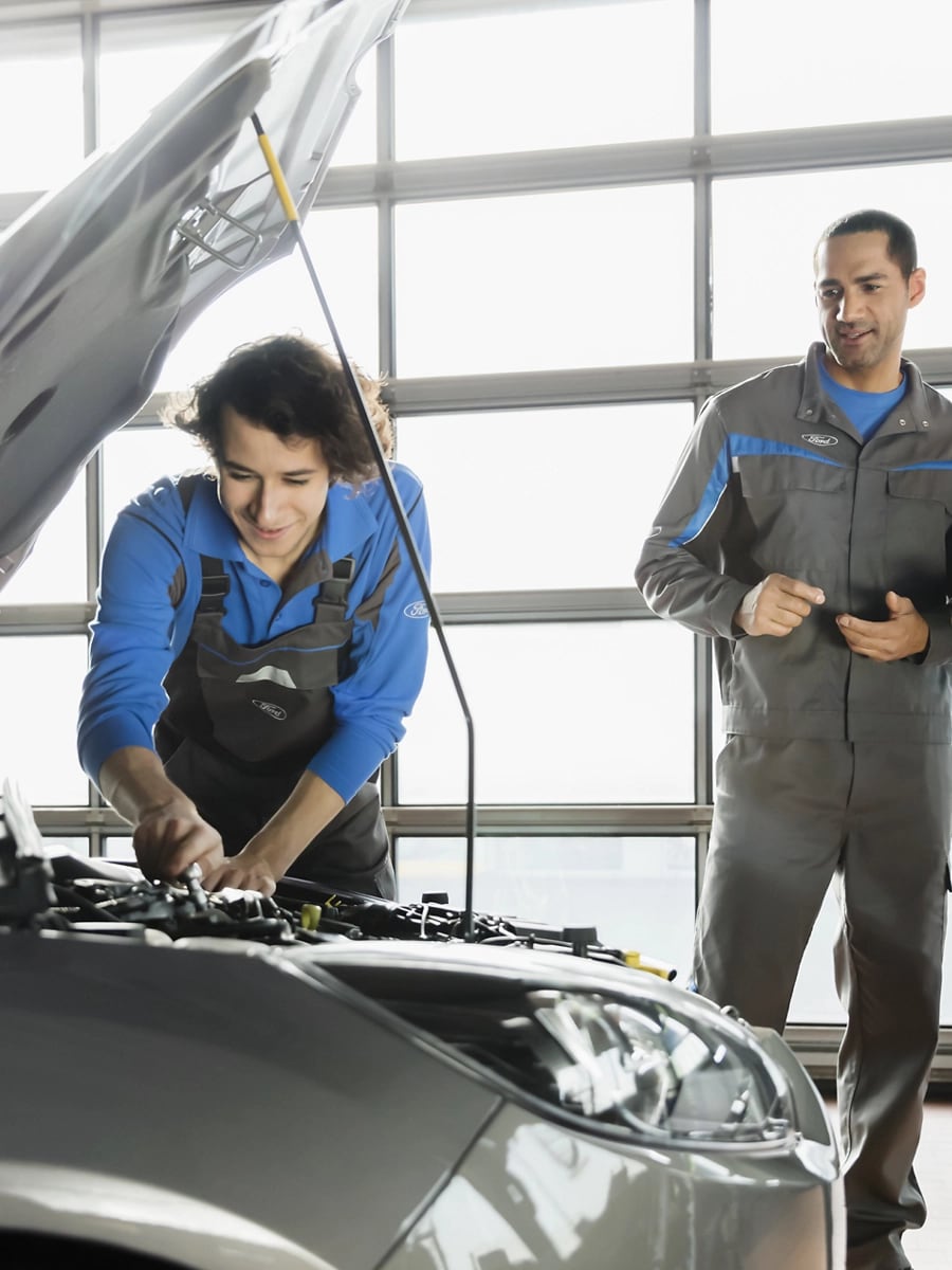 Person works on a vehicle while two others observe.