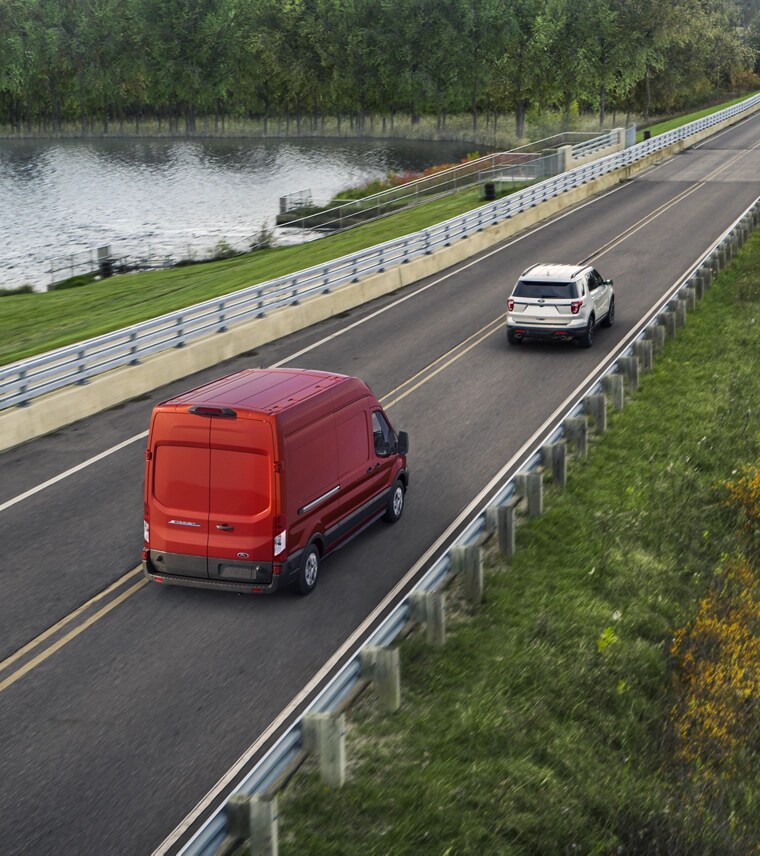 A red 2025 Ford E-Transit™ driving down a country highway