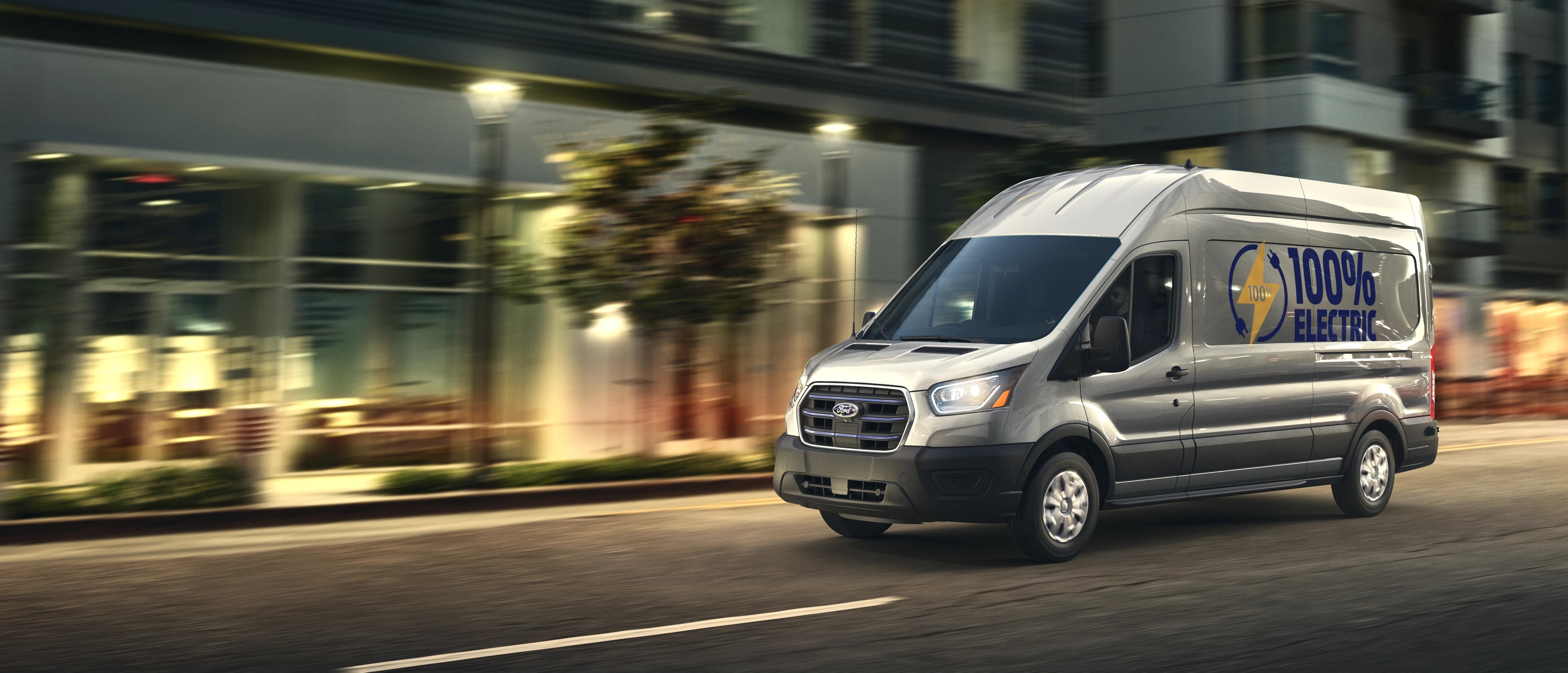 A grey 2025 Ford E-Transit™ van being driven down a city street