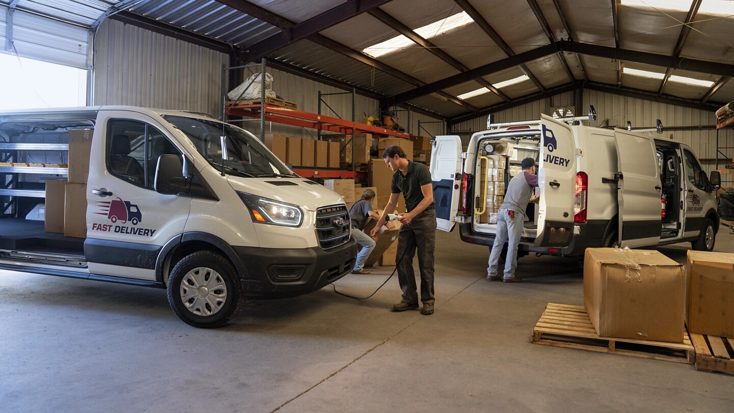 A white 2025 Ford E-Transit™ van parked in a warehouse with workers loading cargo