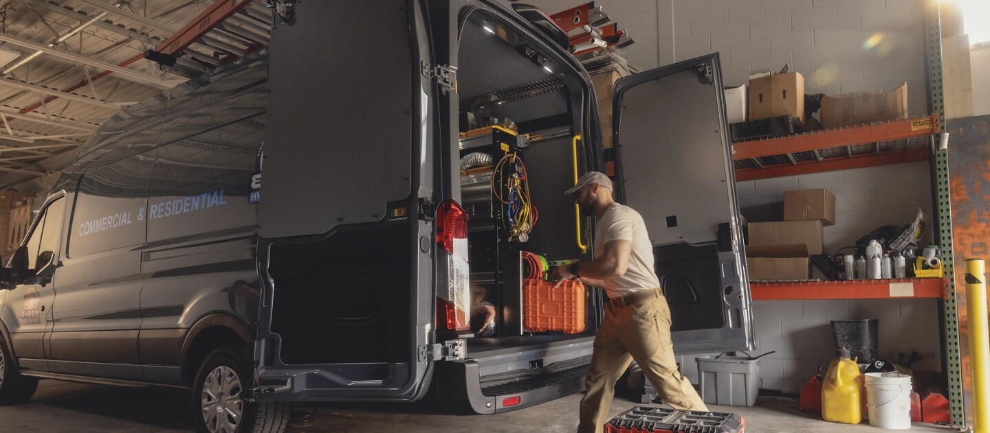 A blue 2025 Ford E-Transit™ van parked in a warehouse as a tradesperson loads gear