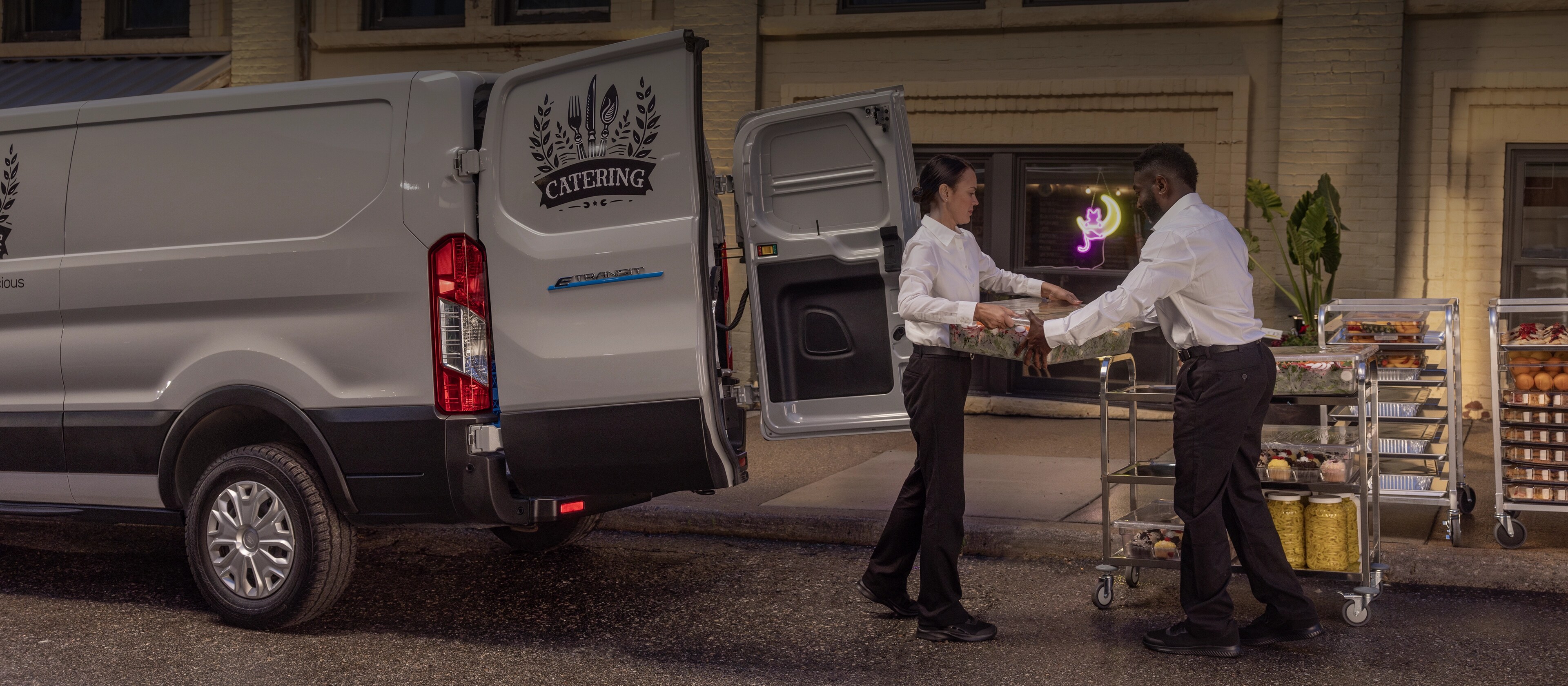 A grey 2025 Ford E-Transit™ van parked and being unloaded at a catering event