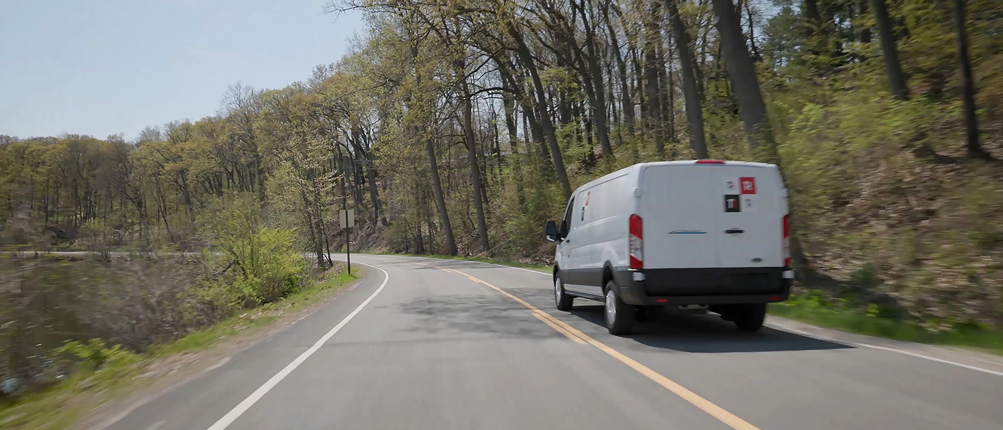 A white 2025 Ford E-Transit™ van being driven through a wooded terrain