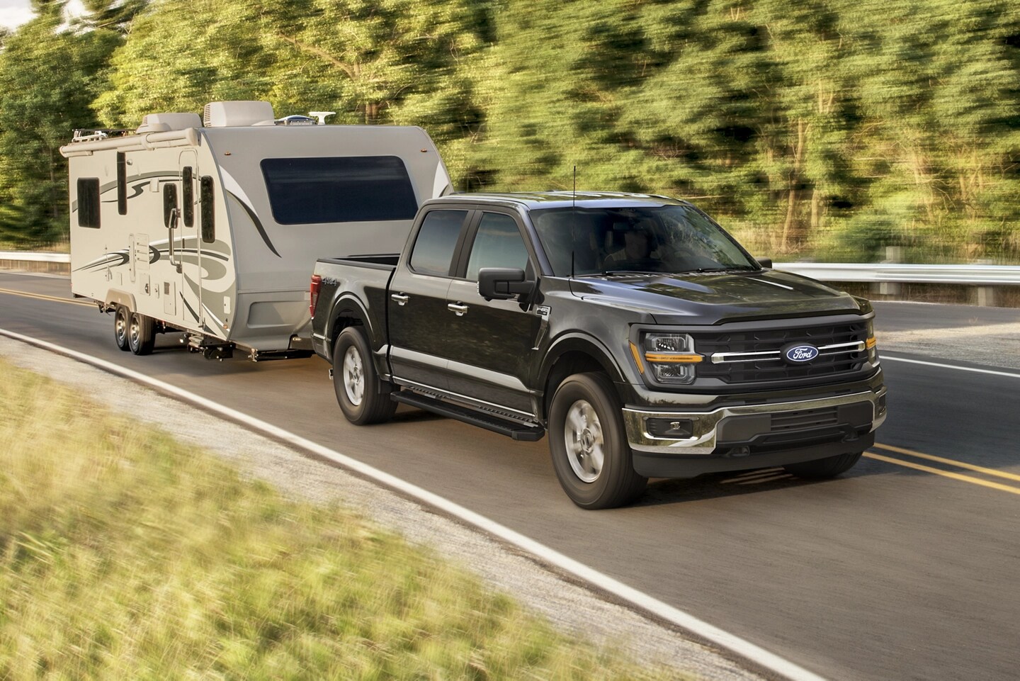 A black Ford F-150® driving along a highway with a trailer attached to the trunk.