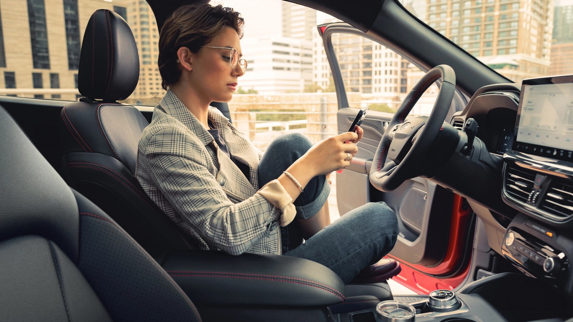 Person using their phone while sitting in a parked 2026 Ford Escape® SUV with the door open