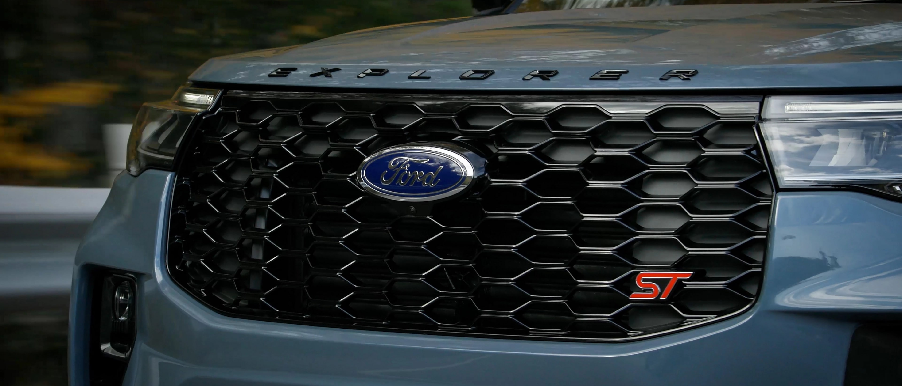 A 2025 Ford Explorer ST in Vapour Blue Metallic driving on a dirt road through a hilly and forested terrain