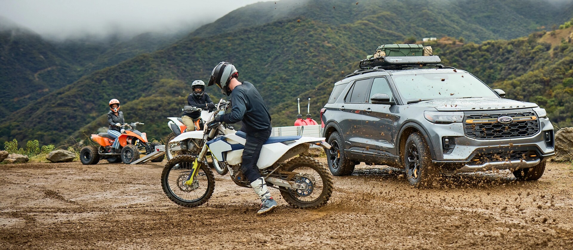 Three people riding dirtbikes through the mud near a 2026 Ford Explorer® SUV