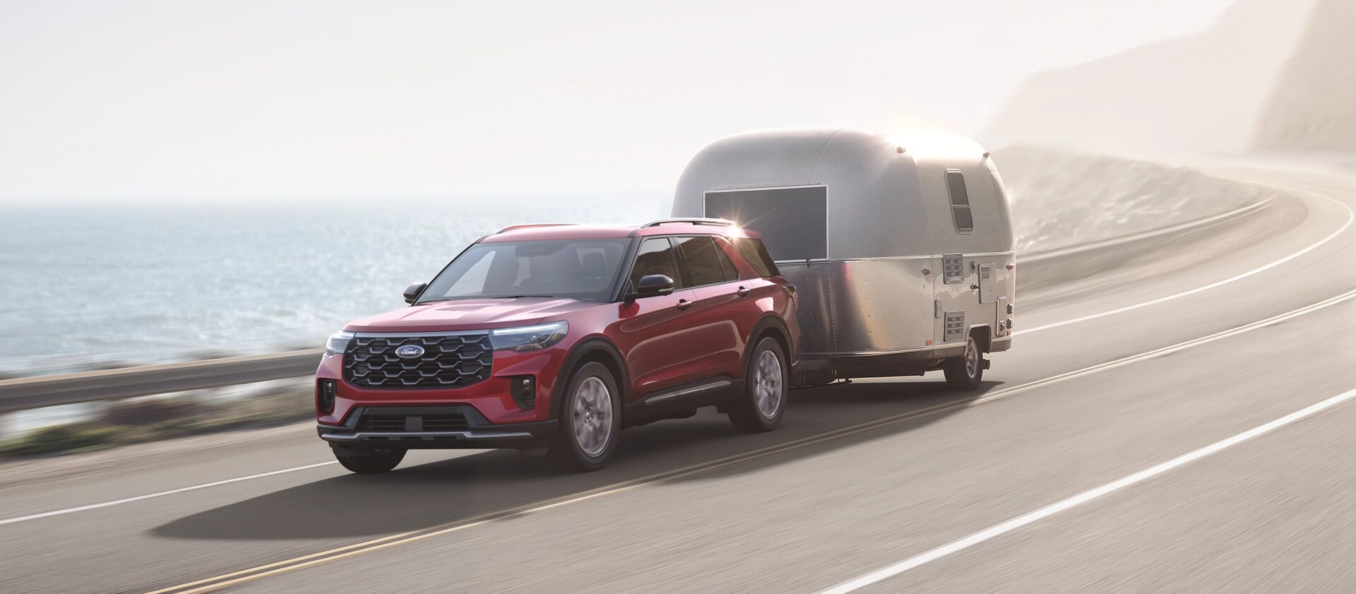 A 2026 Ford Explorer® SUV towing a travel trailer on an oceanside highway