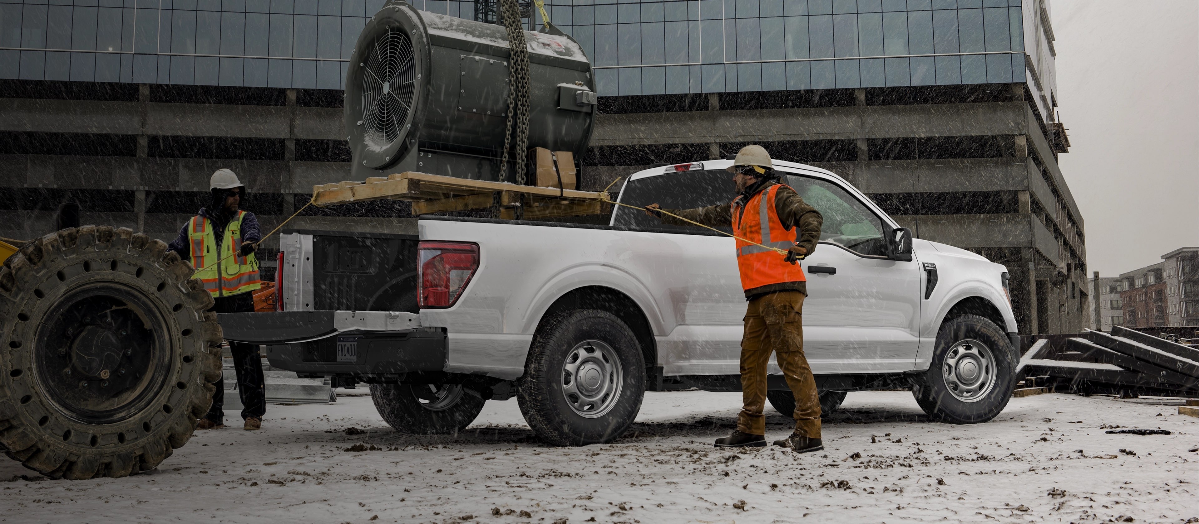 Two construction workers tie down cargo in the bed of a 2025 Ford F-150® pickup parked on a worksite