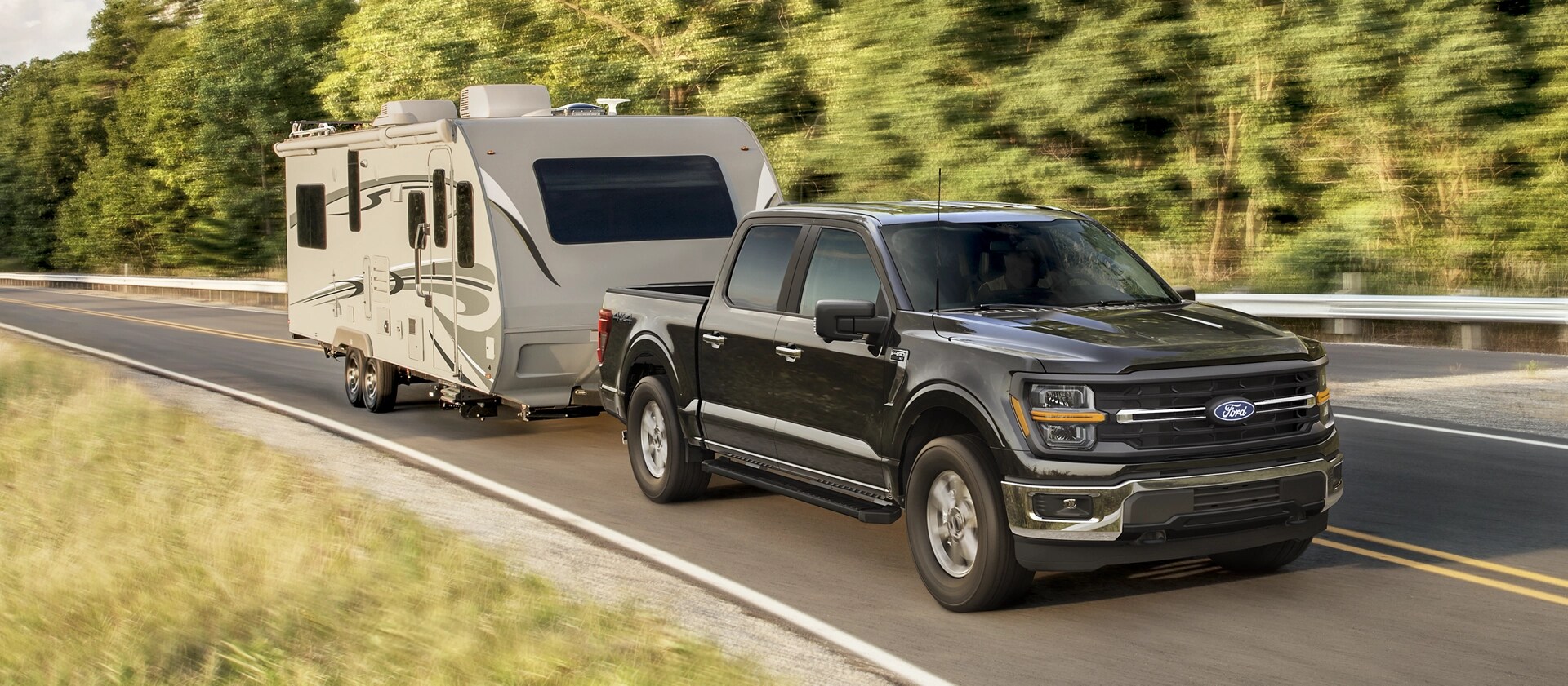 2025 Ford F-150® XLT pickup pulling a camper on a tree-lined road