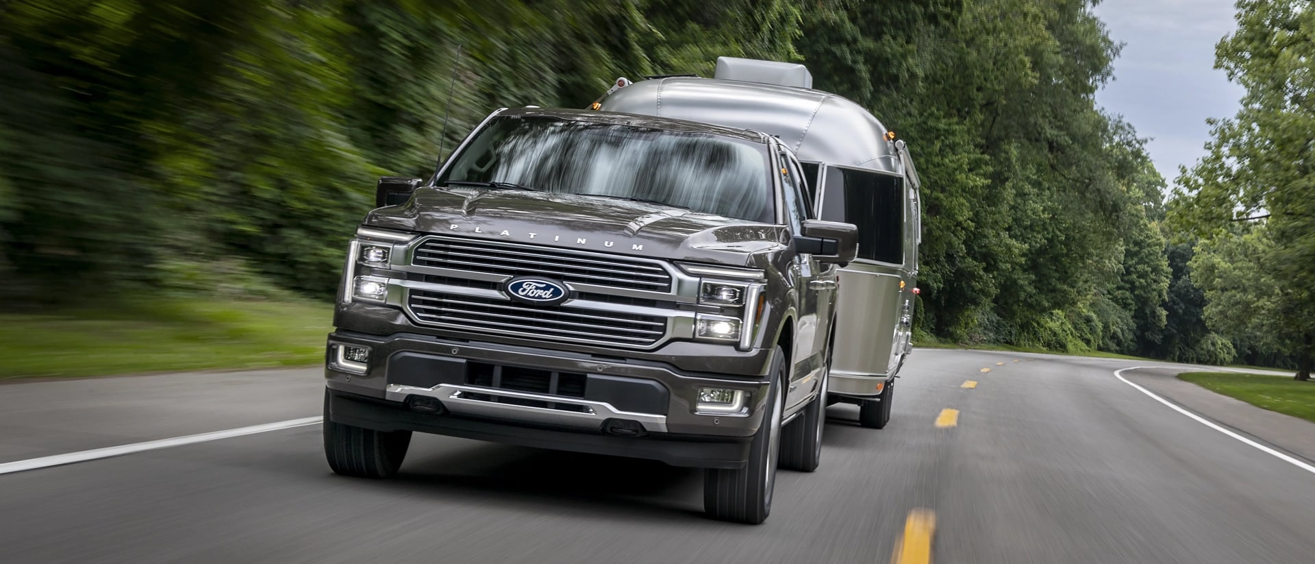 2025 Ford F-150® Platinum® pickup pulling a camper on a tree-lined highway