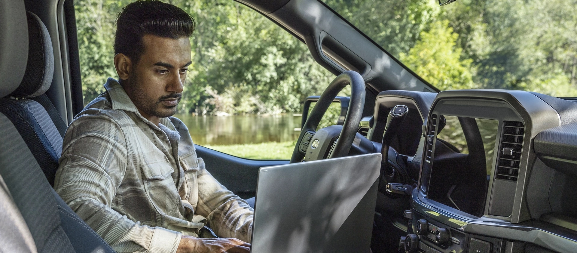 Person sitting in a 2025 Ford F-150® cab working on a laptop computer using the Interior Work Surface 