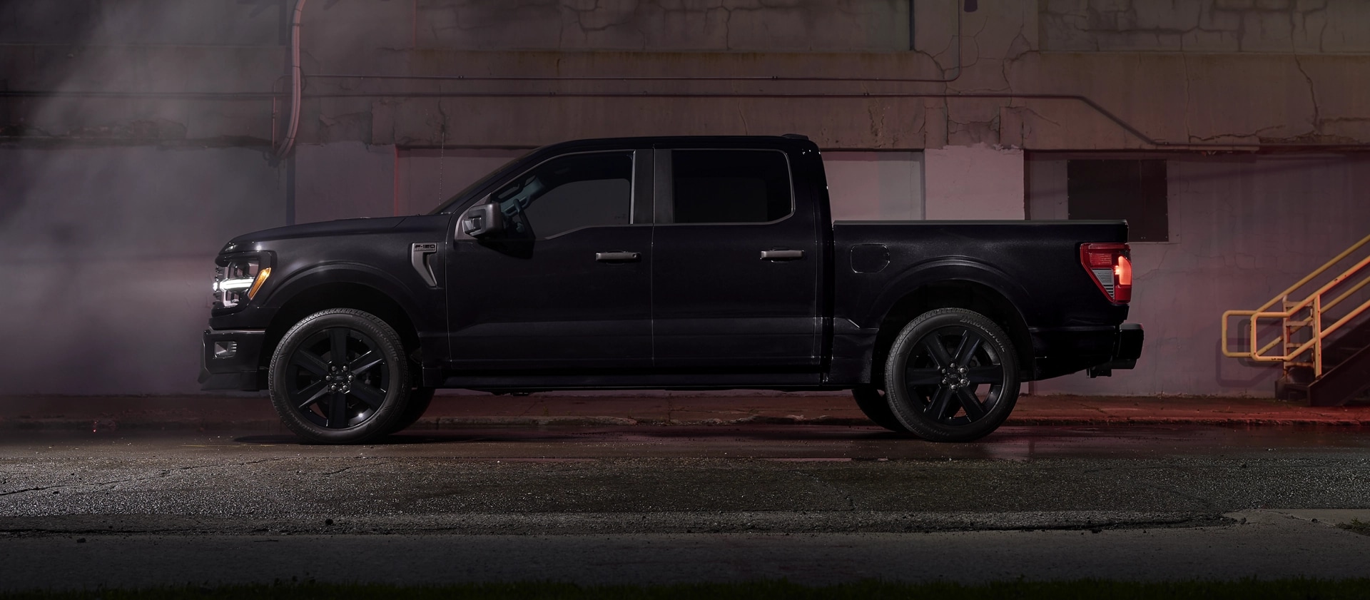 A black 2025 Ford F-150® STX with Lobo™ Package pickup parked near a city building at night