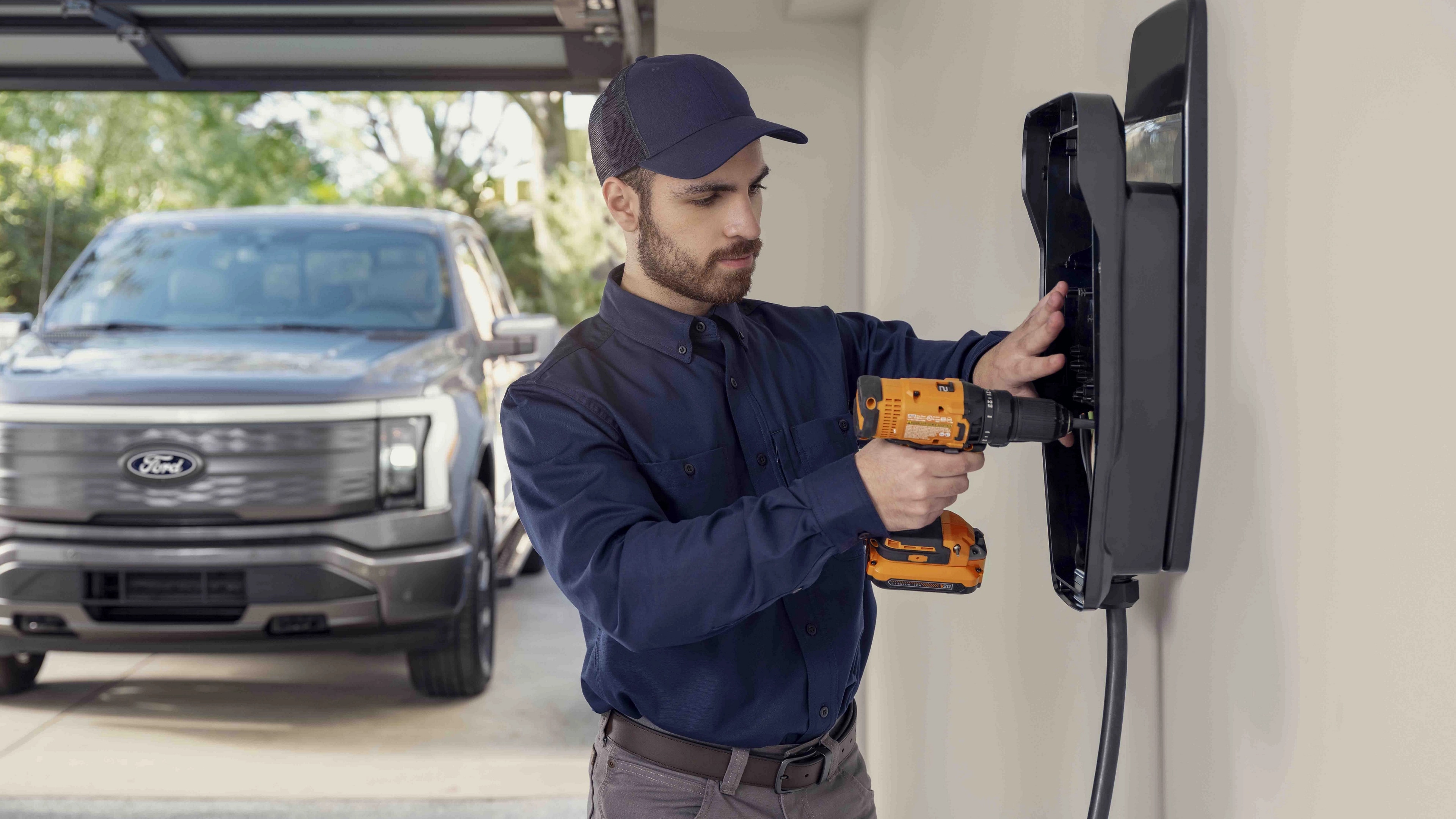 A man installing a home charging station in a garage, with a 2025 Ford F-150® Lightning® pickup parked outside the door
