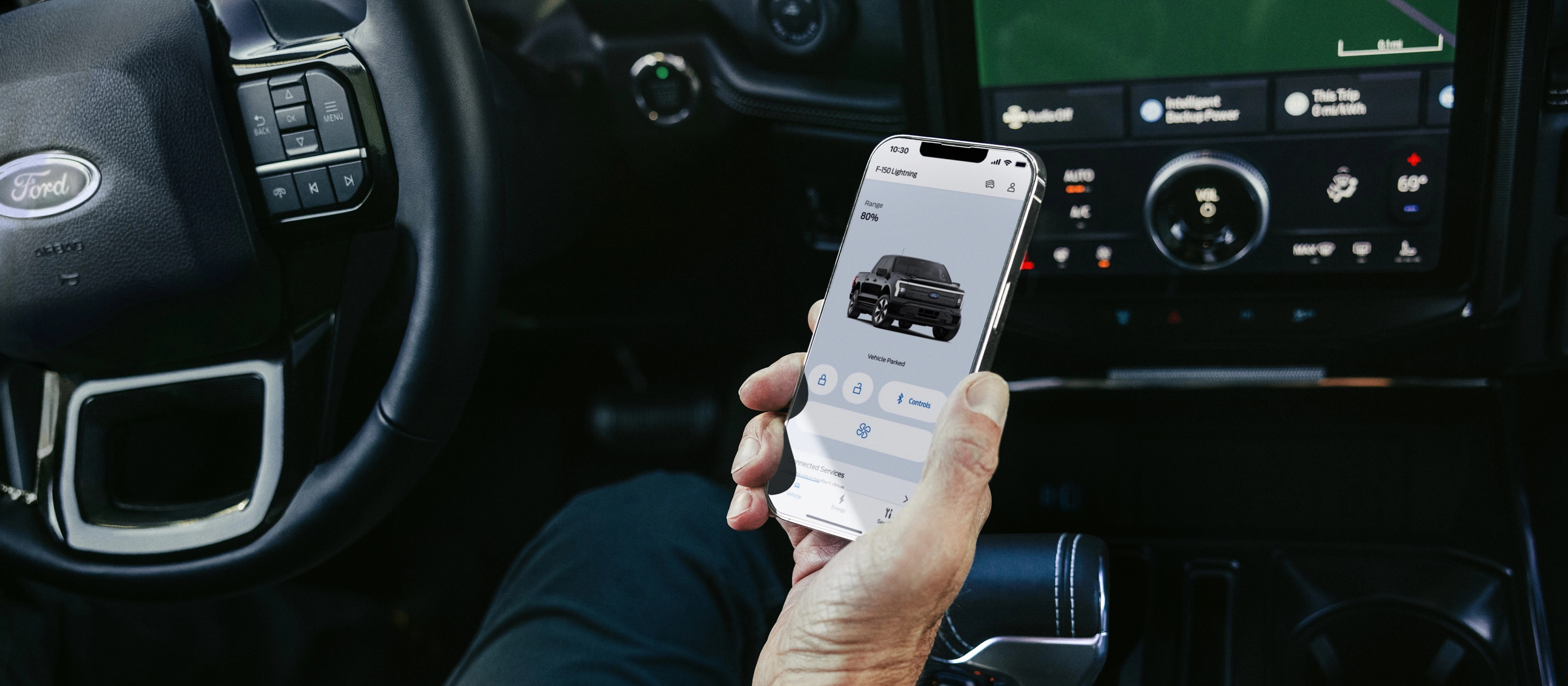 The hand of a driver seated in a 2025 Ford F-150® Lightning® pickup, holding a smartphone showing the FordPass® app