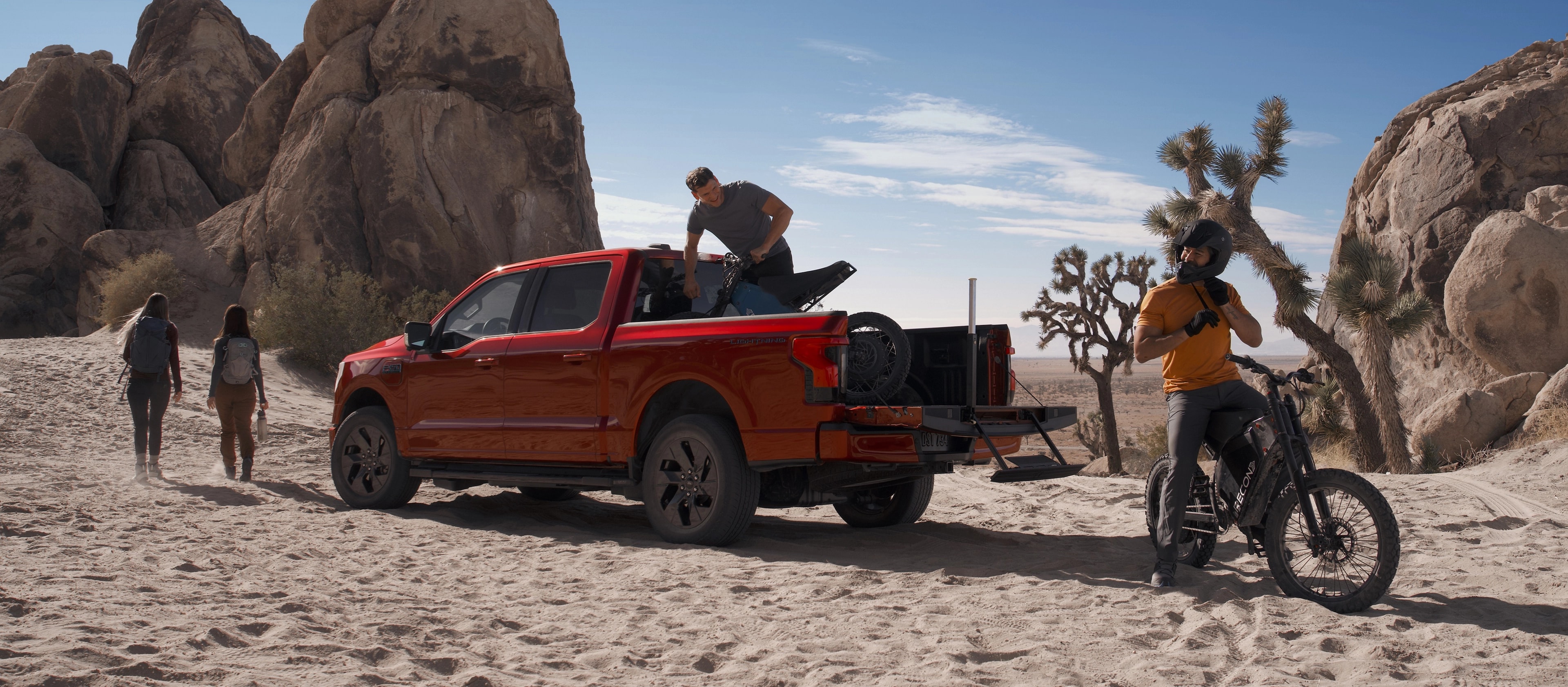 People near a 2025 Ford F-150® Lightning® pickup in the desert, with a dirtbike in the bed and one unloaded