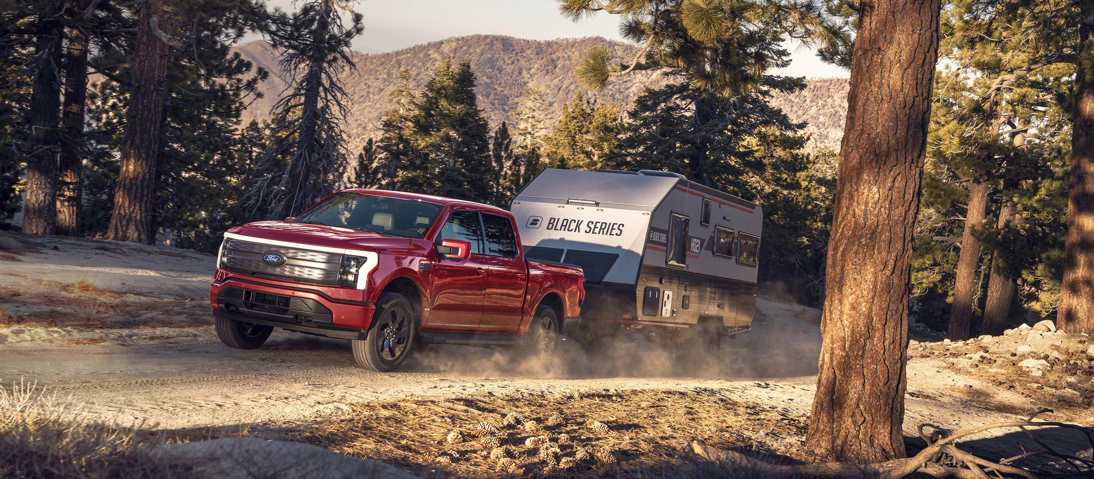 A 2025 Ford F-150® Lightning® is hauling a camper on a dirt road in a scenic location