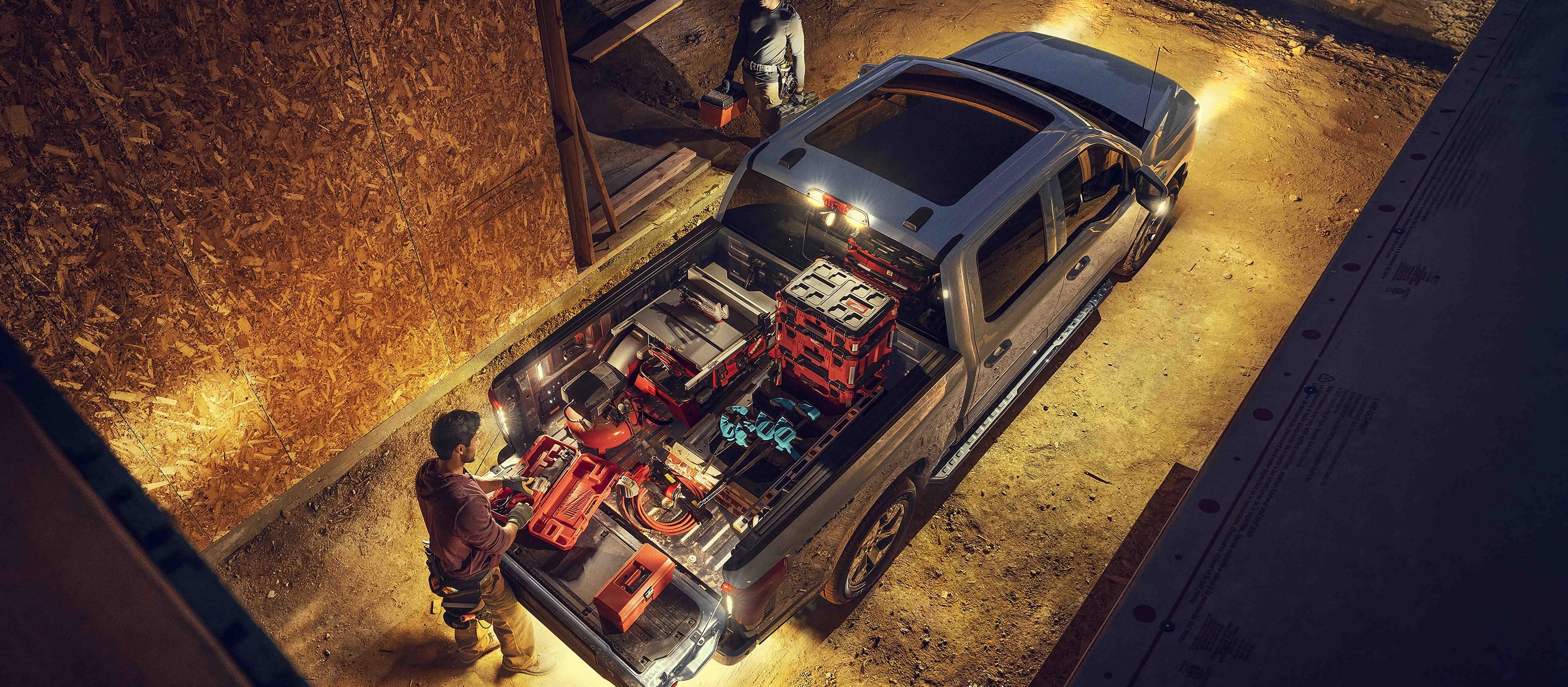 A 2025 Ford F-150® Lightning® lit up at night with a person on a construction site grabbing gear from the truck bed