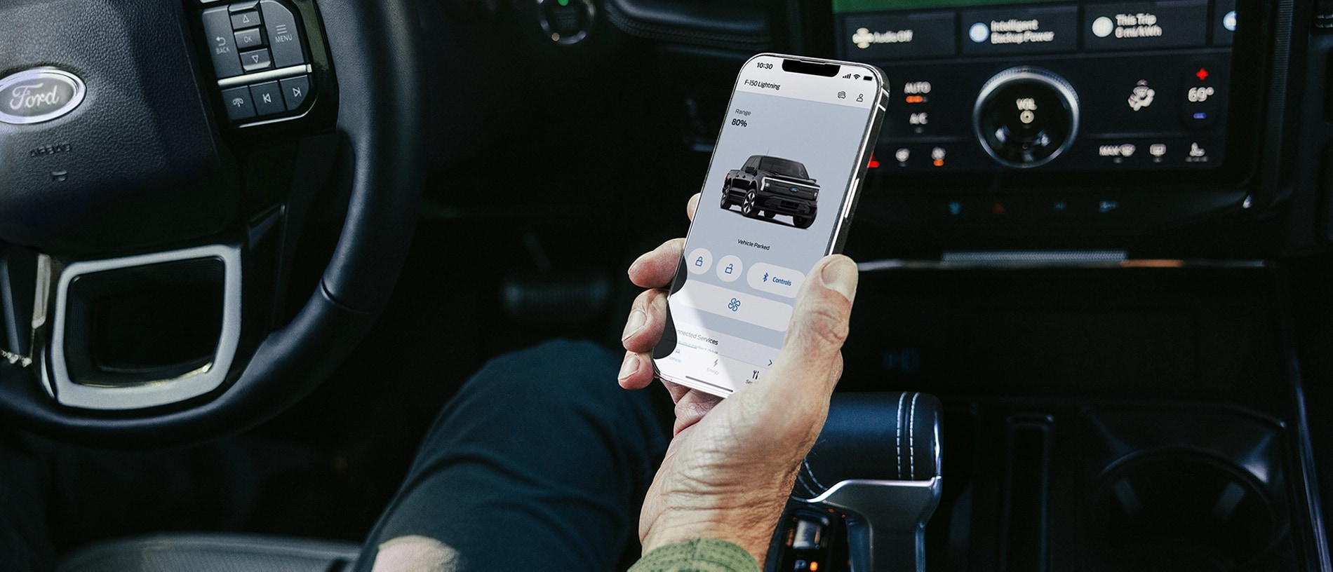 The hand of a driver seated in a 2025 Ford F-150® Lightning® pickup, holding a smartphone showing the FordPass® app