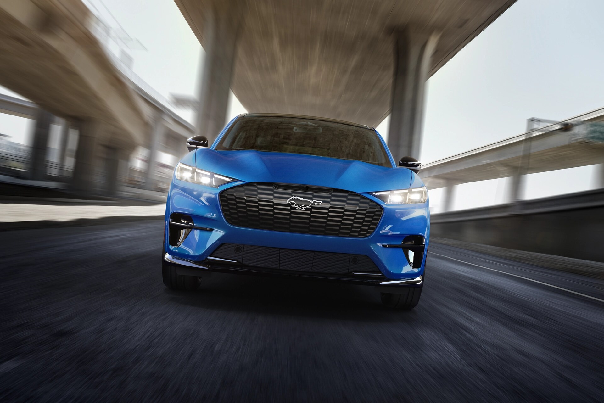 Front view of a 2025 Mustang Mach-E® GT model being driven on a freeway with a blurred background