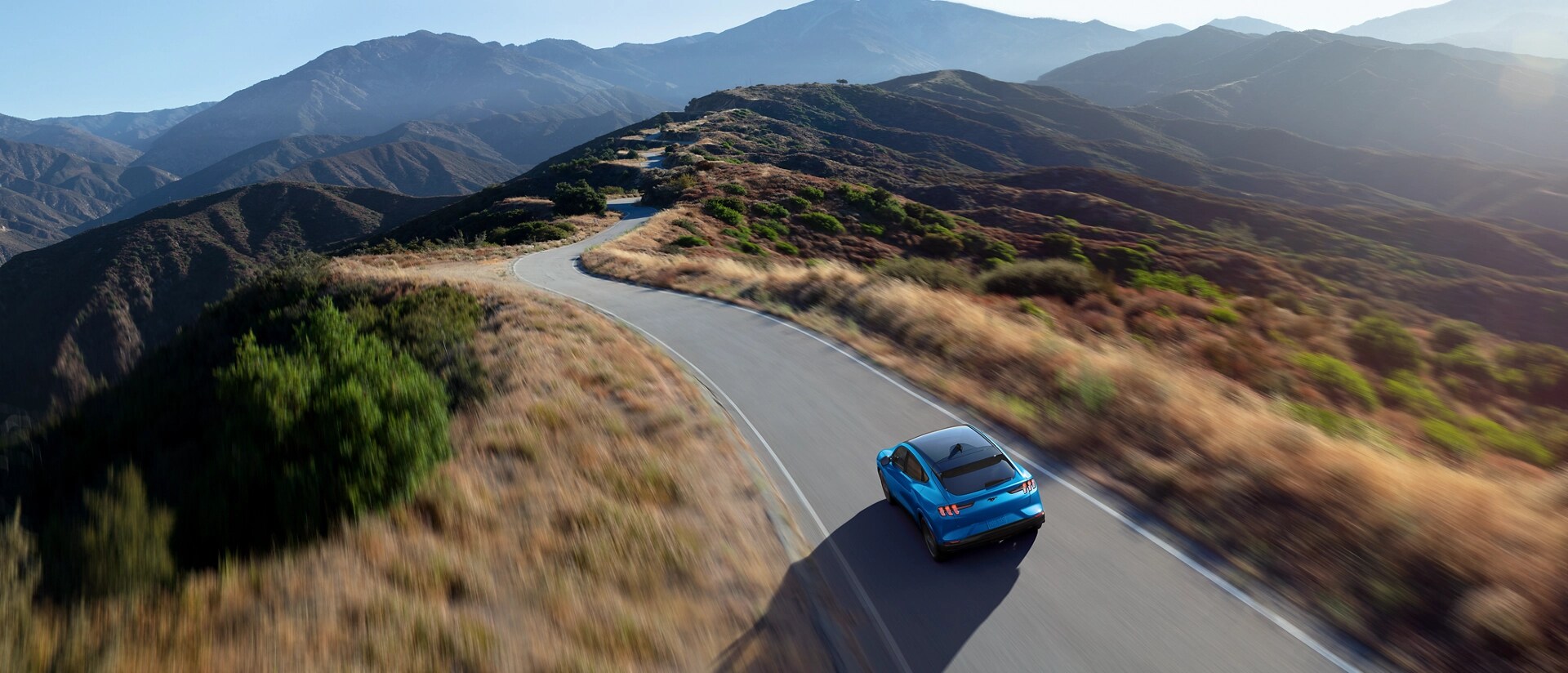 Aerial view of a 2025 Ford Mustang Mach-E® being driven on a scenic road through mountains