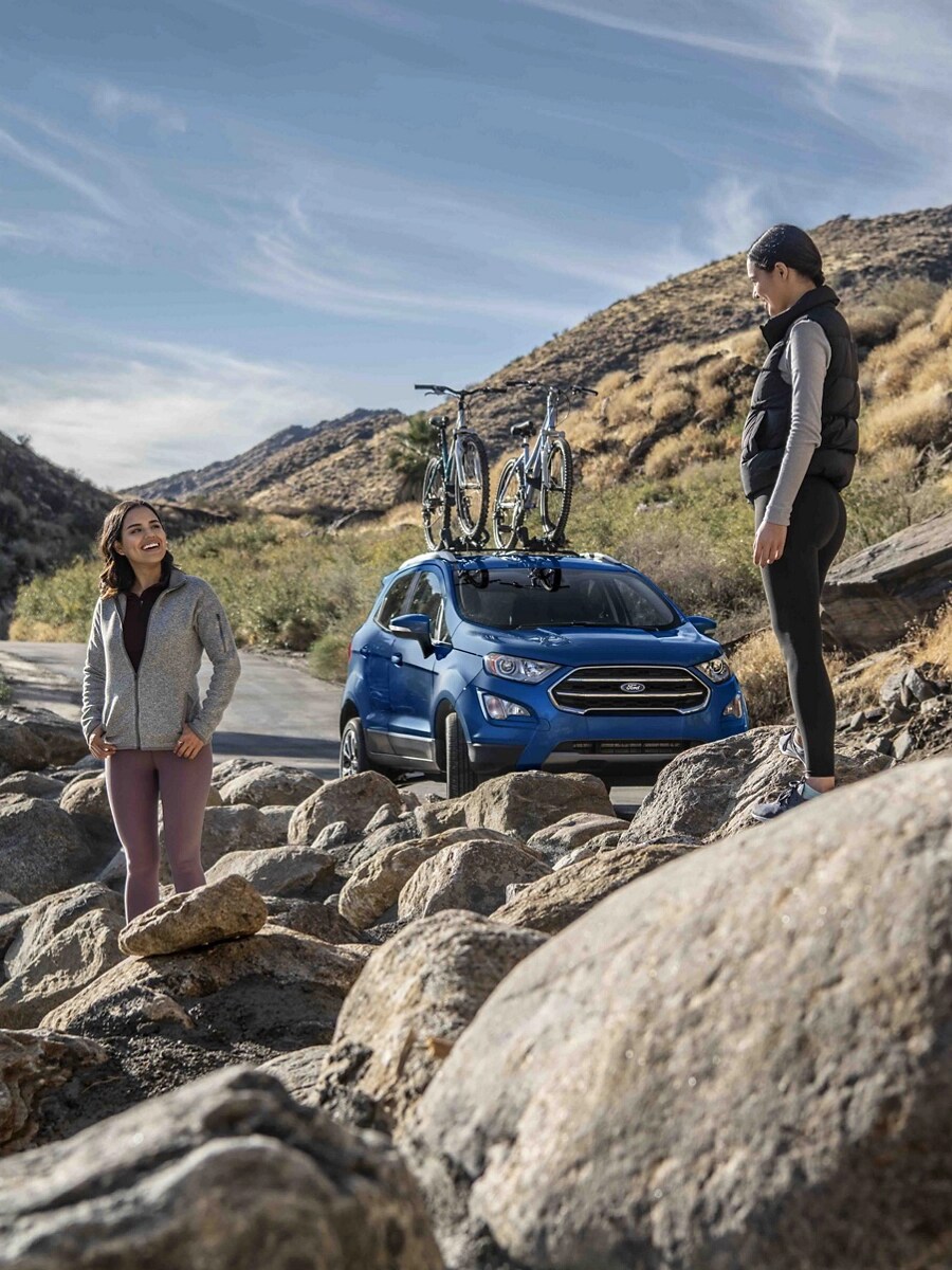 Two young women stand in a rocky landscape near a Ford crossover