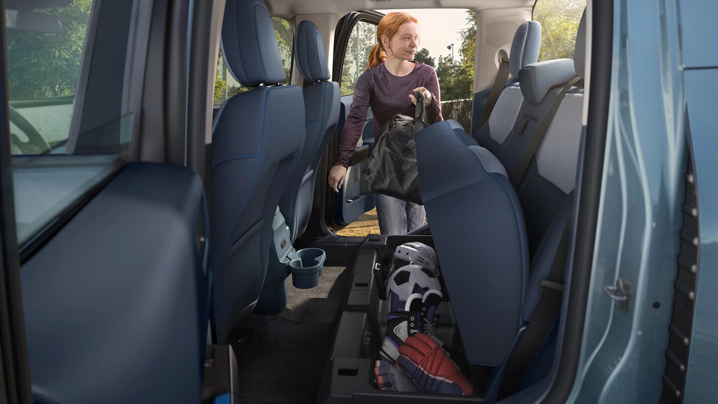 A woman putting a bag into the under-seat storage on a 2025 Ford Maverick® pickup
