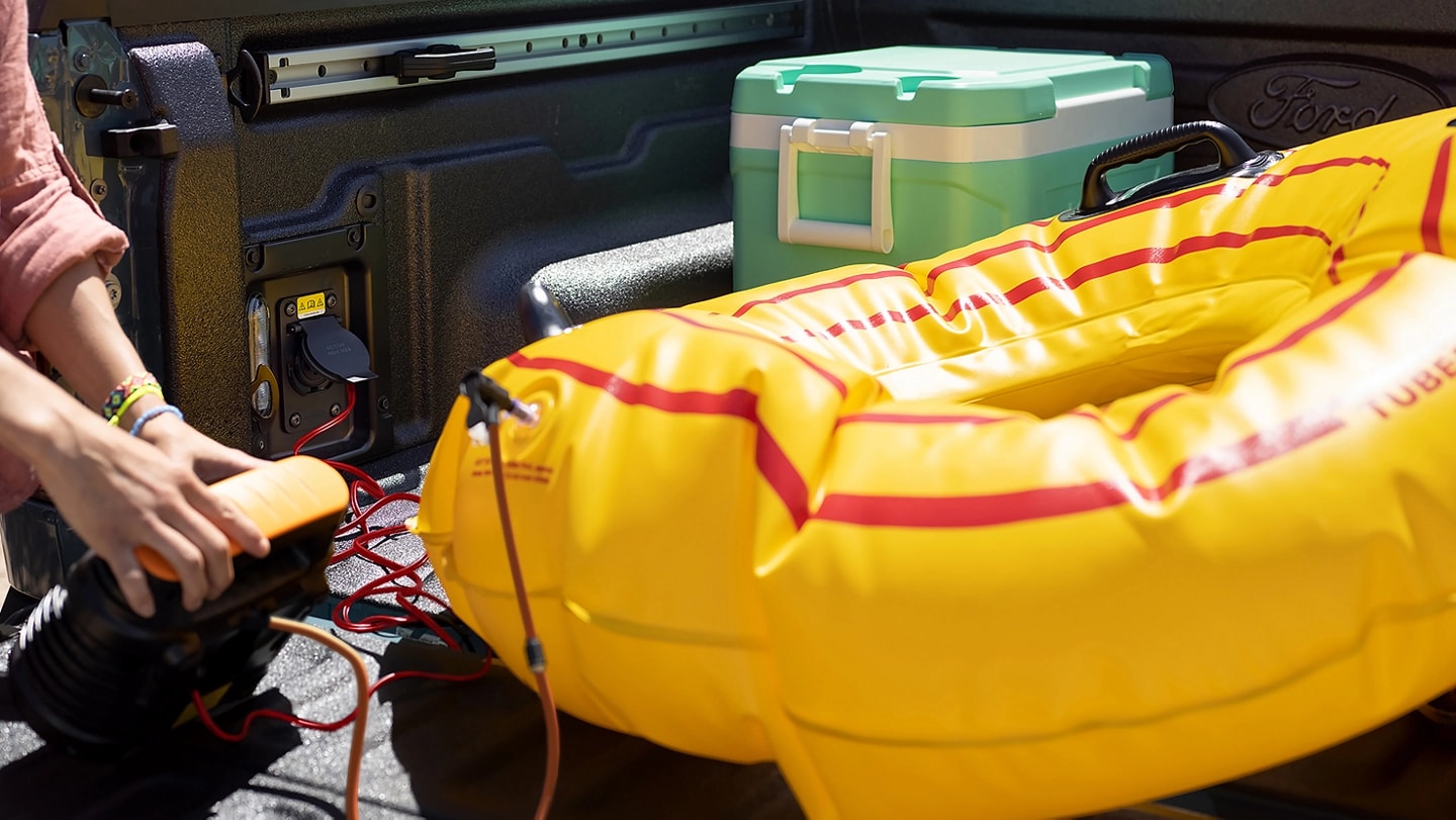 A person using an air pump to inflate a raft. Using an available outlet in the cargo bed of a 2025 Ford Maverick® pickup