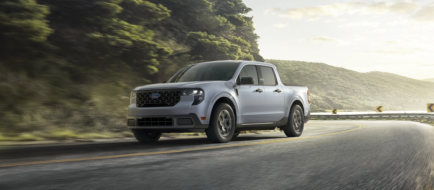 A 2025 Ford Maverick® pickup driving on a winding road near a mountain lake