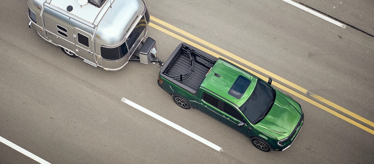 An aerial view of a 2025 Ford Maverick® pickup pulling a travel trailer down a highway