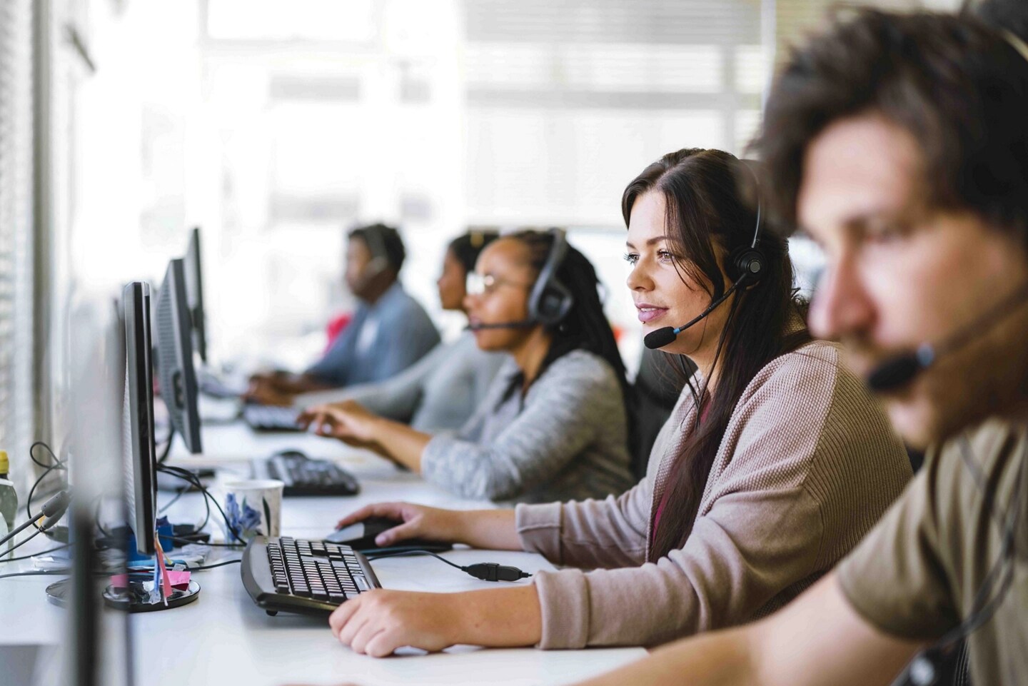 A team of customer service agents, all wearing headsets, seated at a row of computers